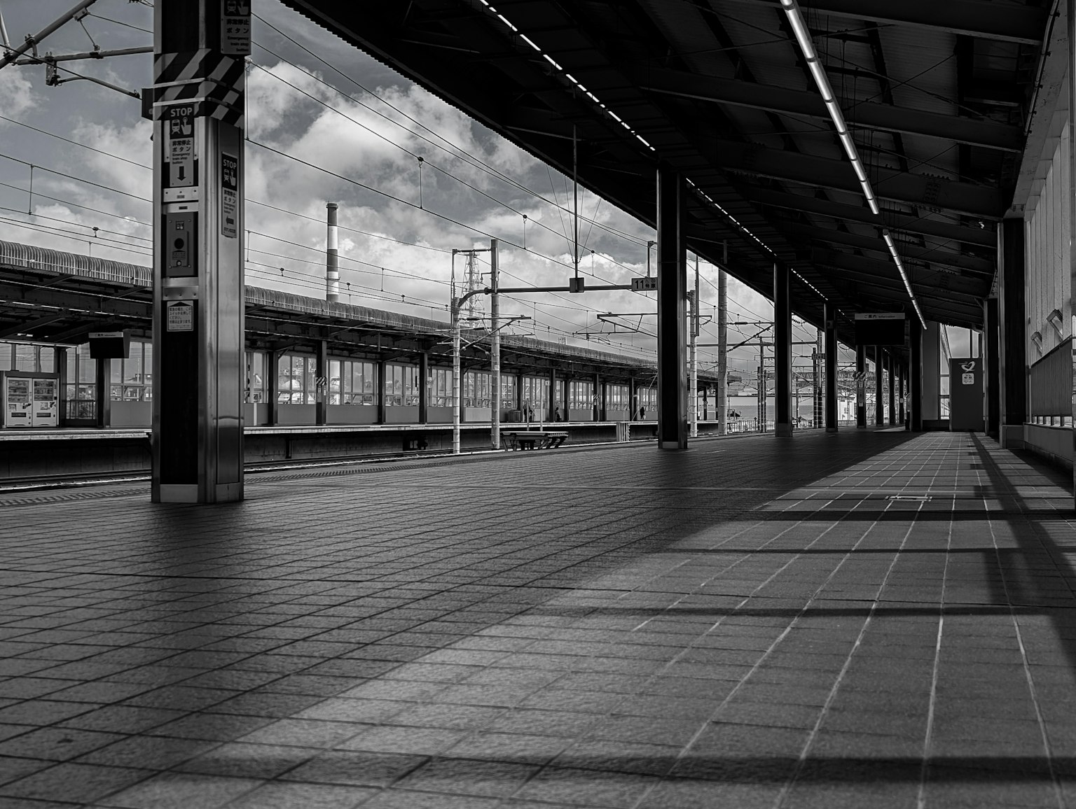 モノクロの駅のプラットフォームが広がる風景 鉄道の線路と雲が見える