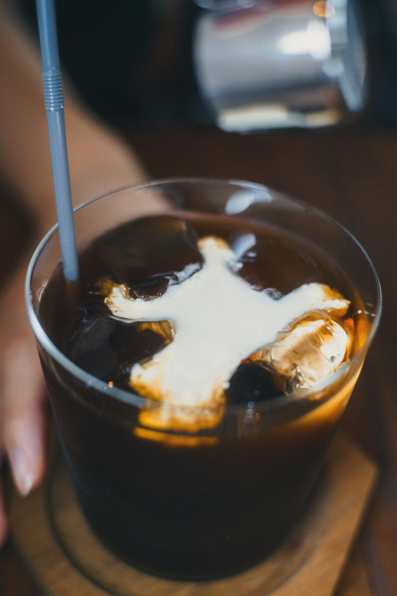 クリームが浮かんだアイスコーヒーのグラス 手に持たれている