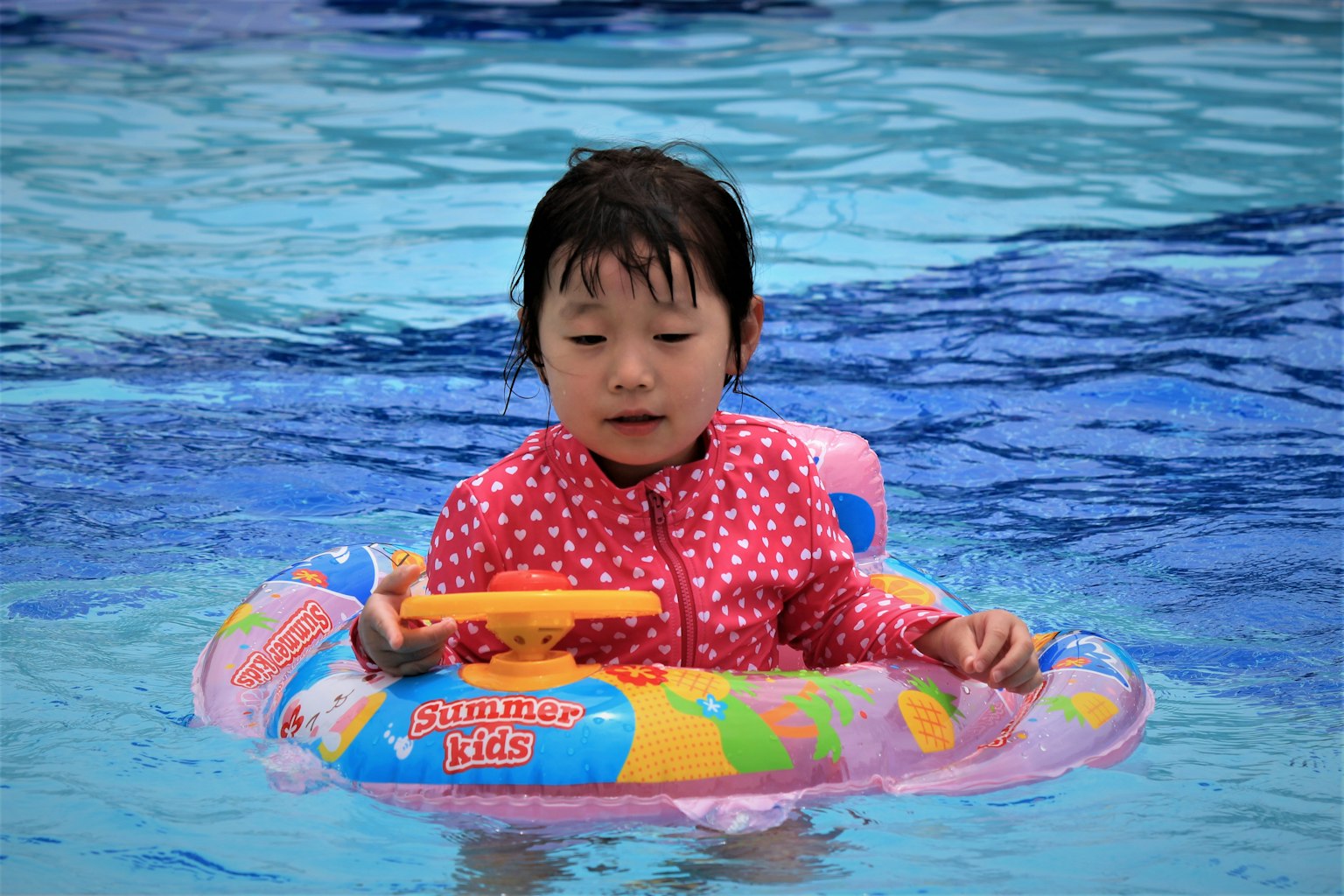 Child playing in water wearing polka dot swimsuit colorful inflatable ring