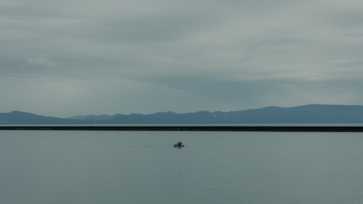 Ein kleines Boot, das auf einem ruhigen See mit entfernten Bergen im Hintergrund schwimmt