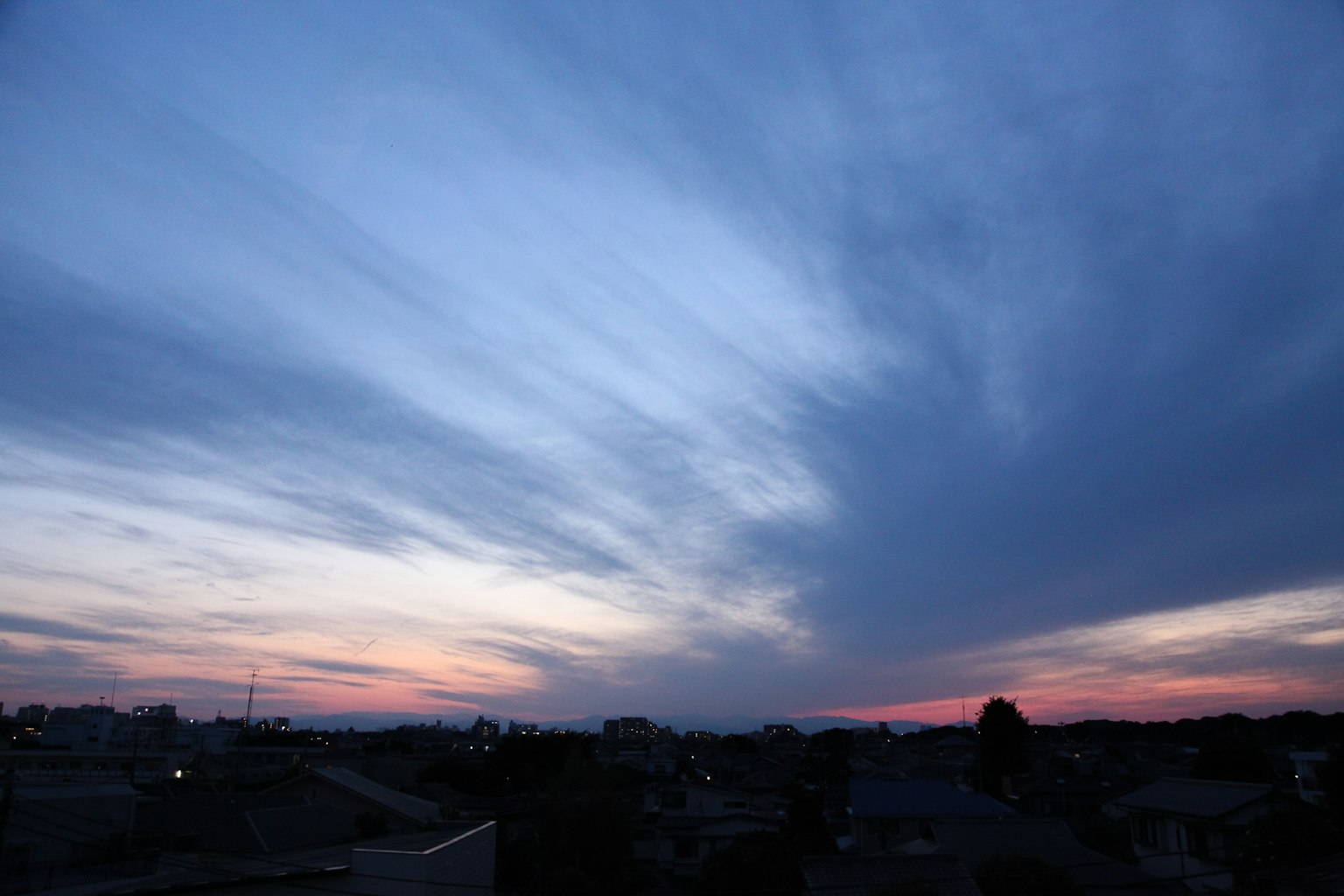 Dramatic sunset sky with streaked clouds and faint city lights