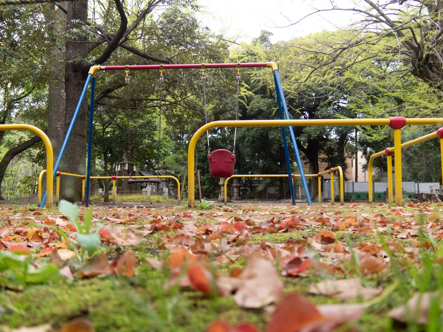 Pemandangan taman bermain dengan ayunan dan daun jatuh di rumput hijau ayunan kuning dan biru