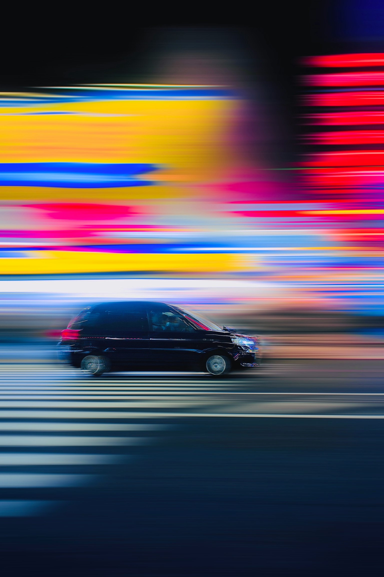 黒い車が横断歩道を通過する夜の都市の風景 明るいネオンの光が背景に広がる