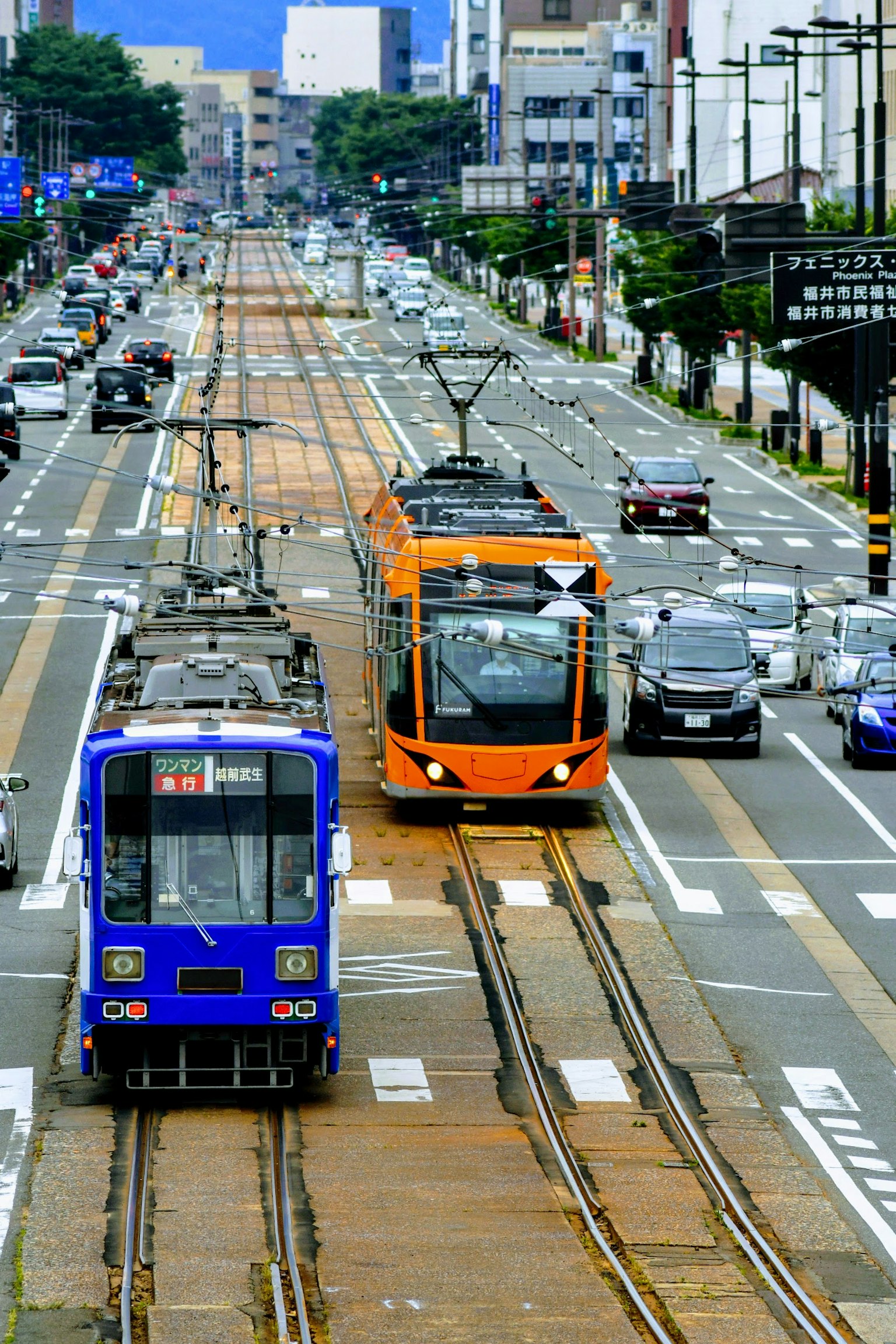 Blaue und orange Straßenbahnen in einer Stadtszene