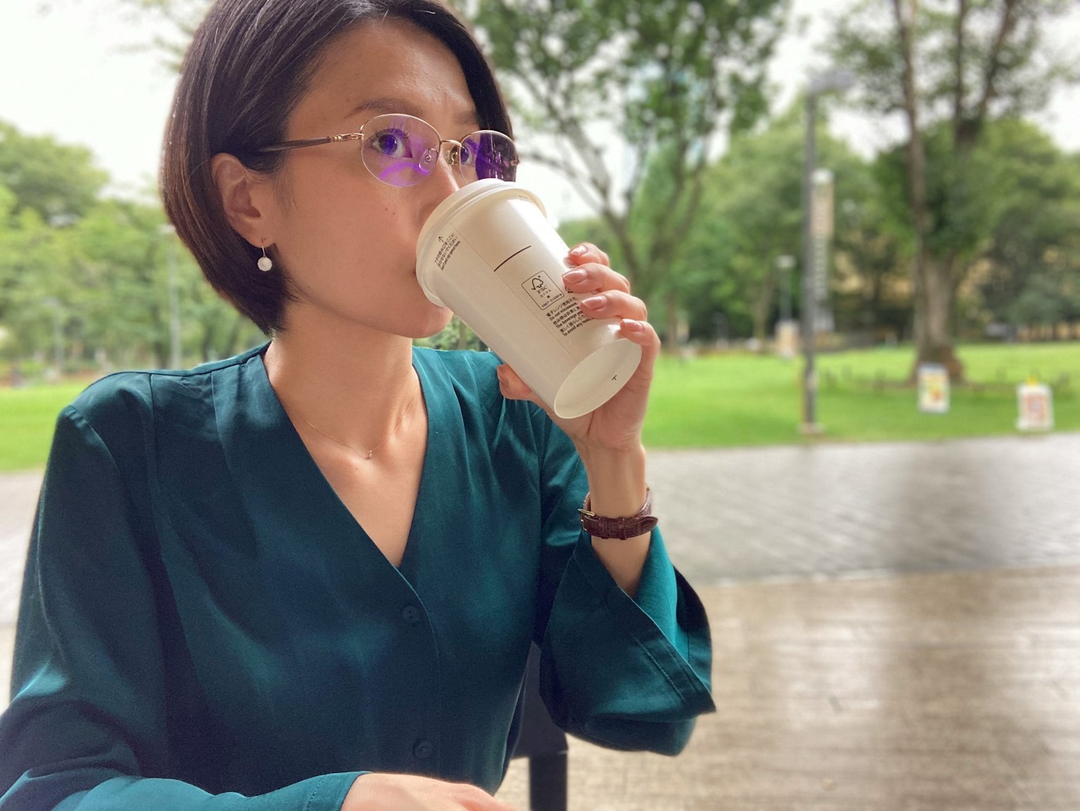 Một người phụ nữ trong áo blouse xanh đang thưởng thức đồ uống tại quán cà phê