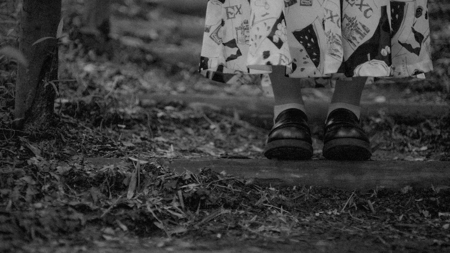 Black and white photo featuring feet in shoes and a patterned skirt