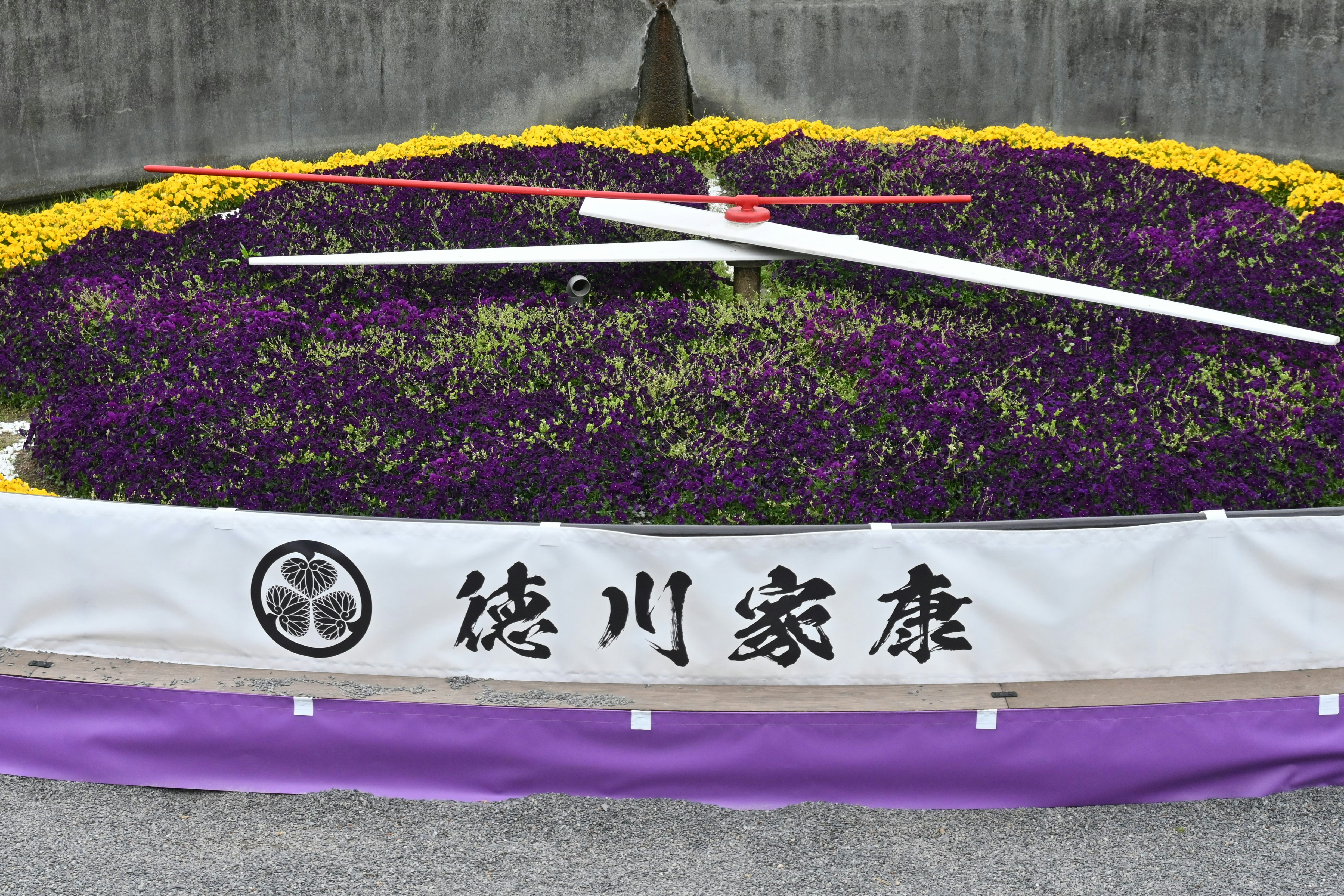 花時計の周囲に咲く花壇と紫の横幕