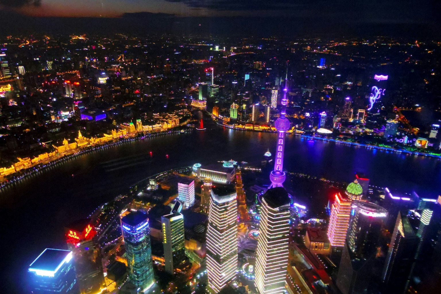 Luftaufnahme der Skyline von Shanghai bei Nacht mit beleuchteten Wolkenkratzern und dem Fluss