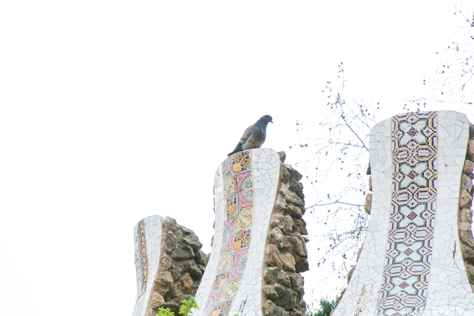 Seekor burung bertengger di atas pilar batu yang dihiasi mozaik