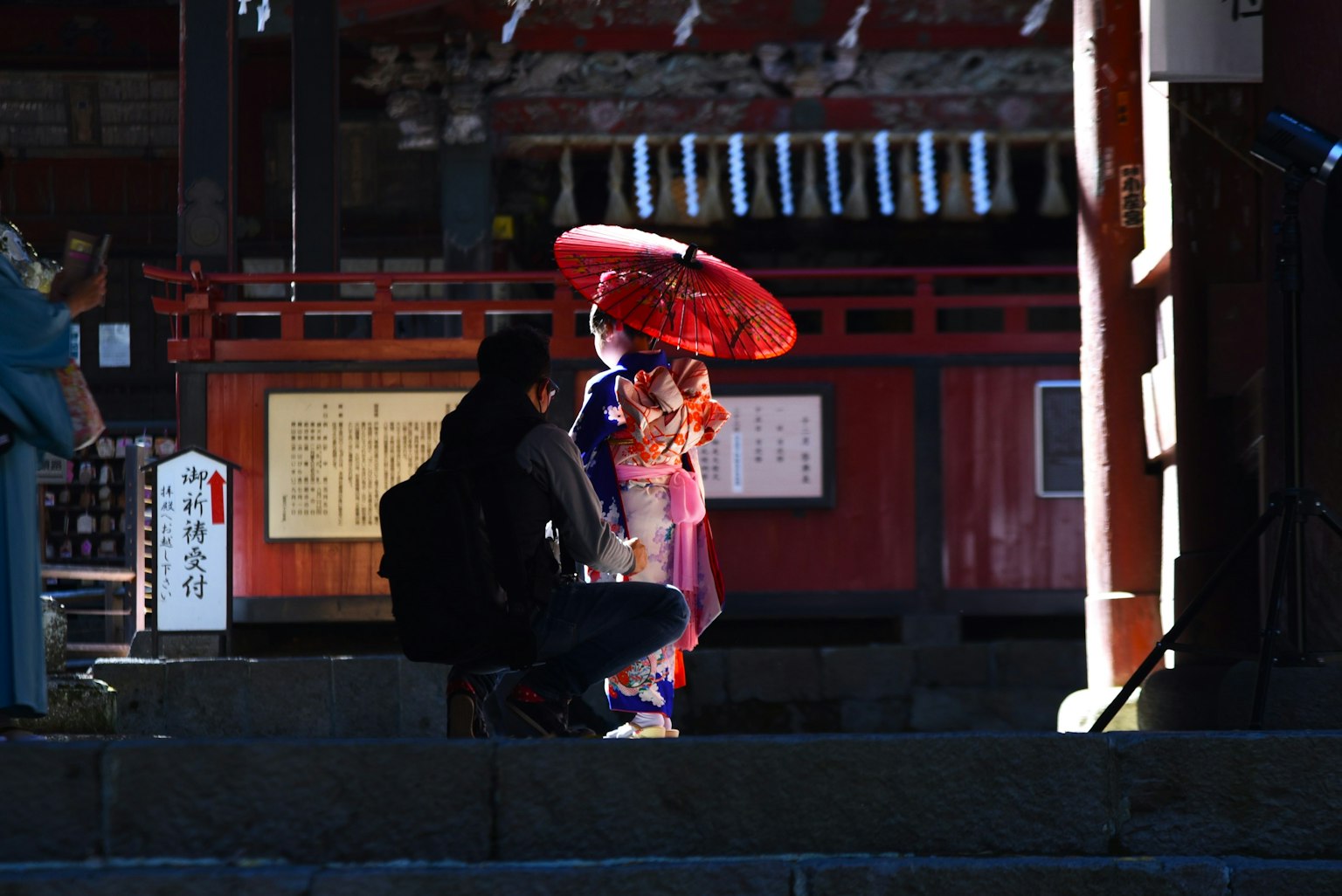 Una donna in kimono con un ombrello rosso si trova davanti a un santuario