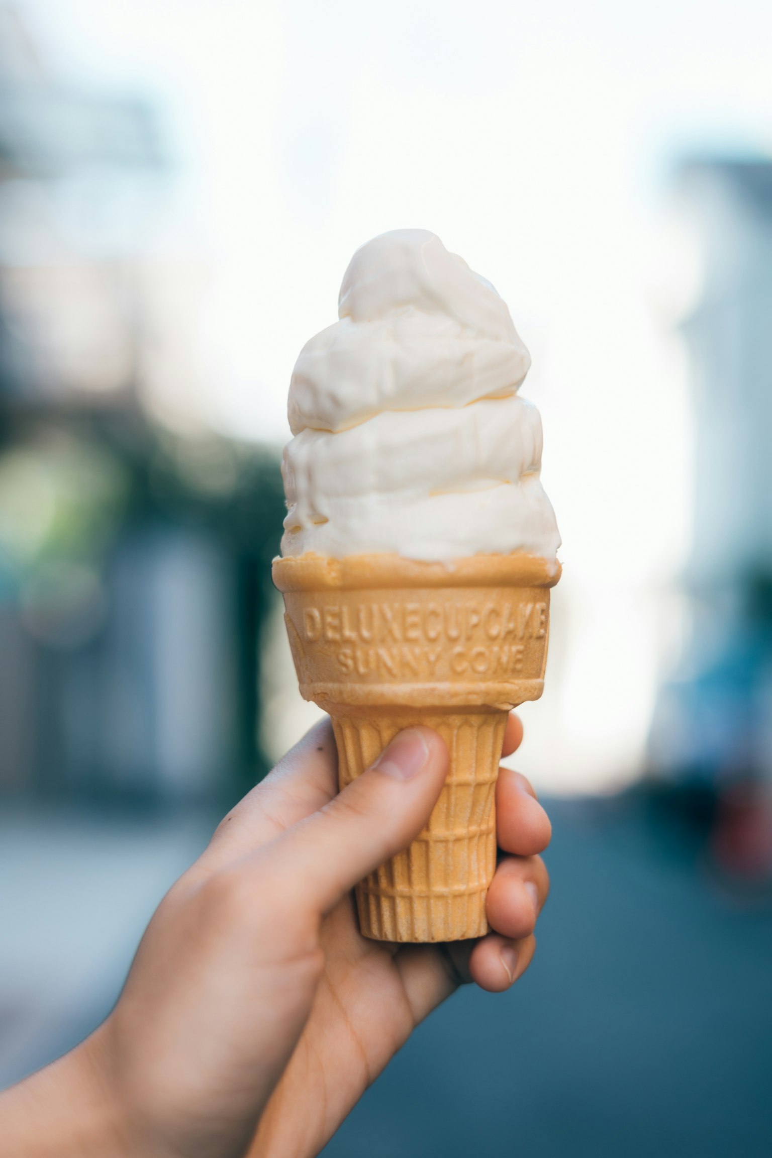 Photo of a hand holding an ice cream cone topped with white ice cream