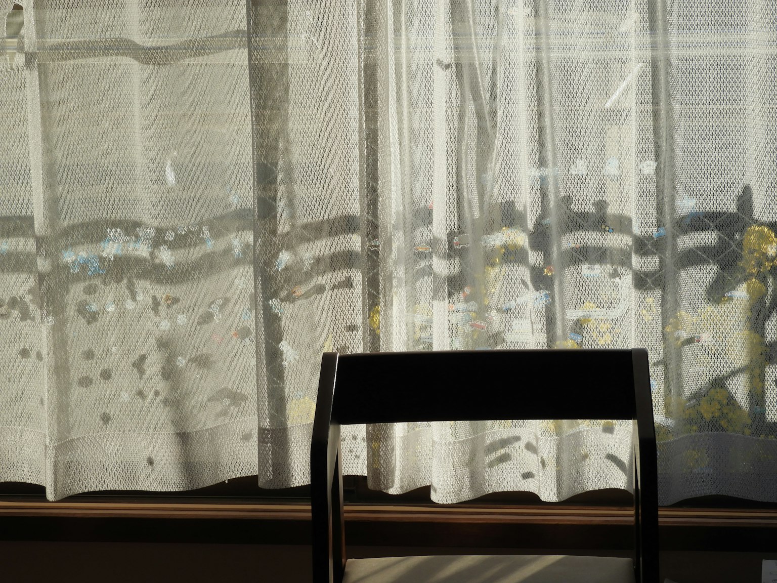 Une scène avec une chaise noire et des rideaux transparents près d'une fenêtre