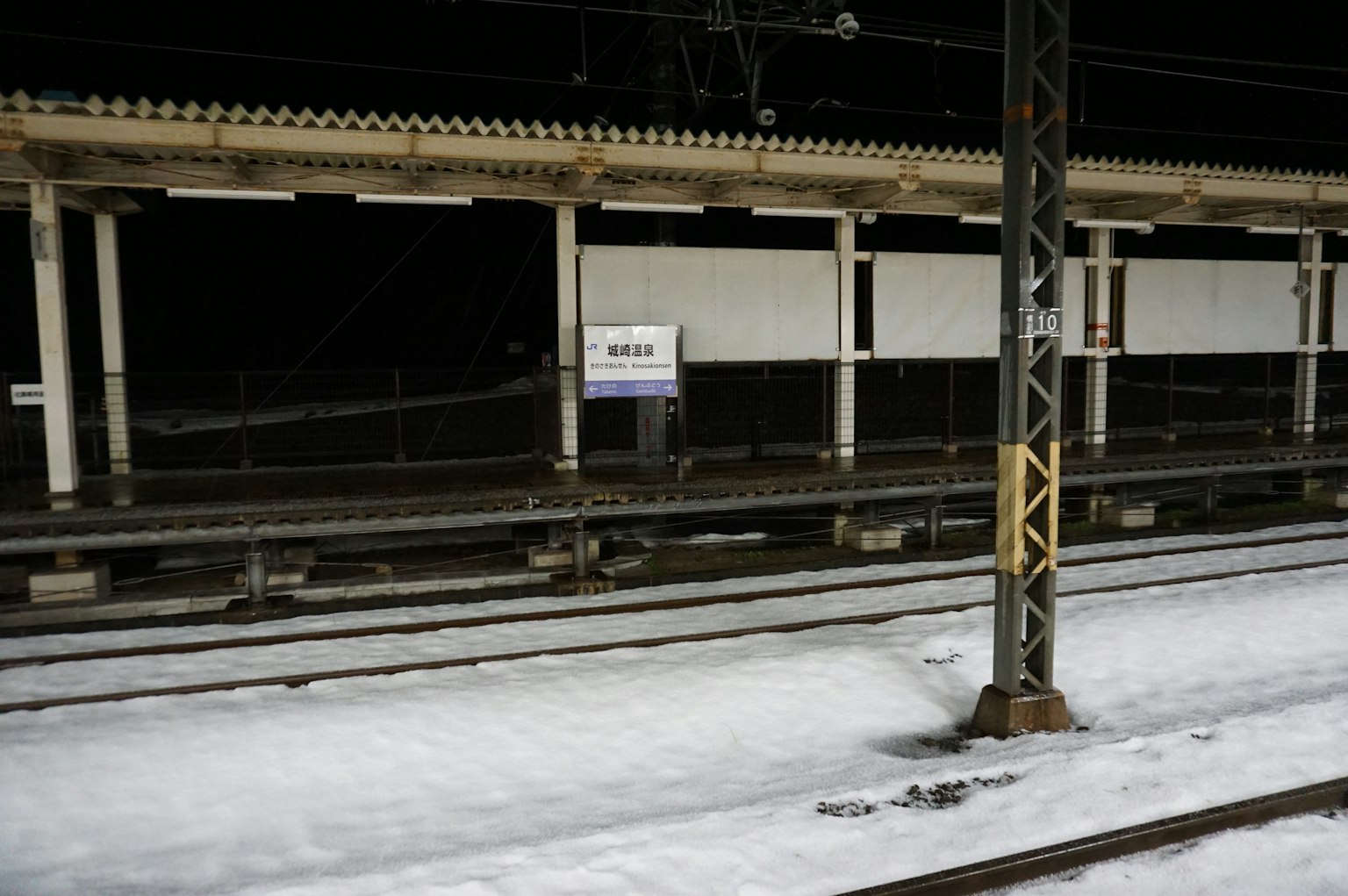 Scena notturna di una piattaforma ferroviaria innevata con binari