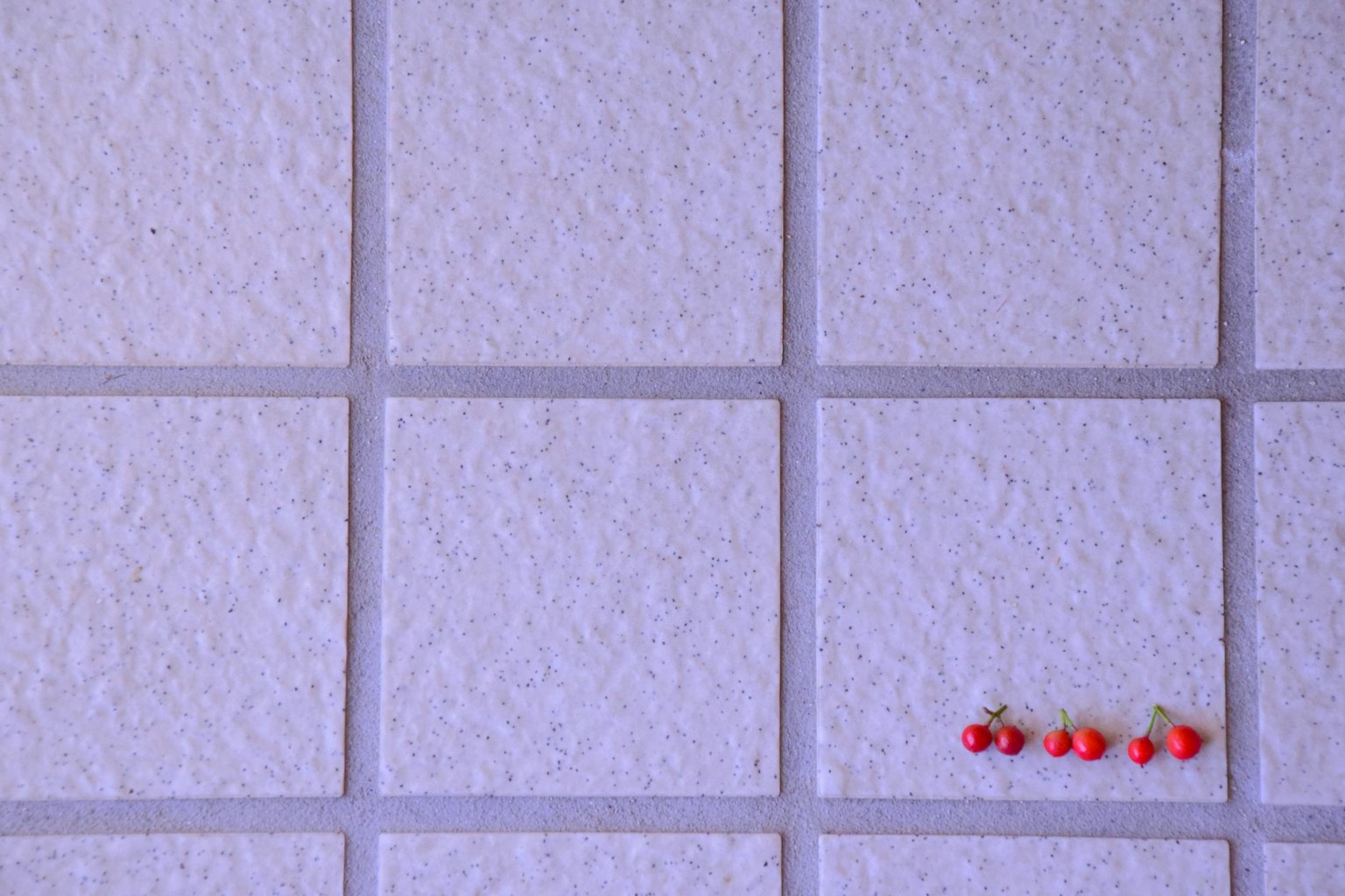 Perle rosse disposte su una superficie piastrellata bianca