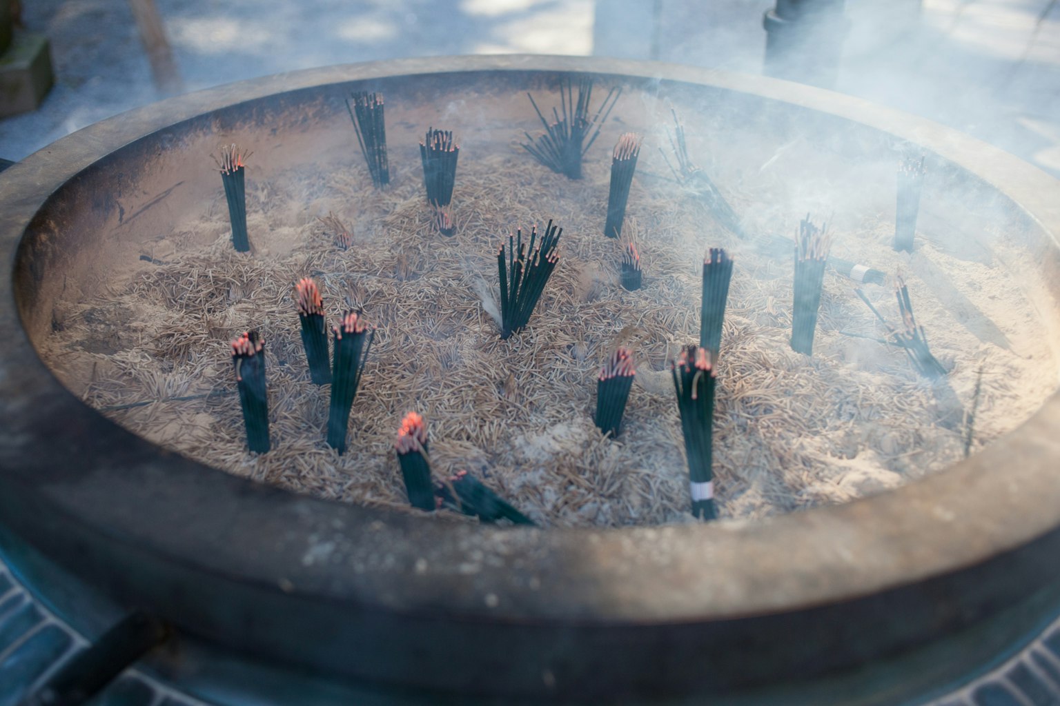 Một chiếc bình lớn chứa đầy que nhang bao quanh bởi tro và khói