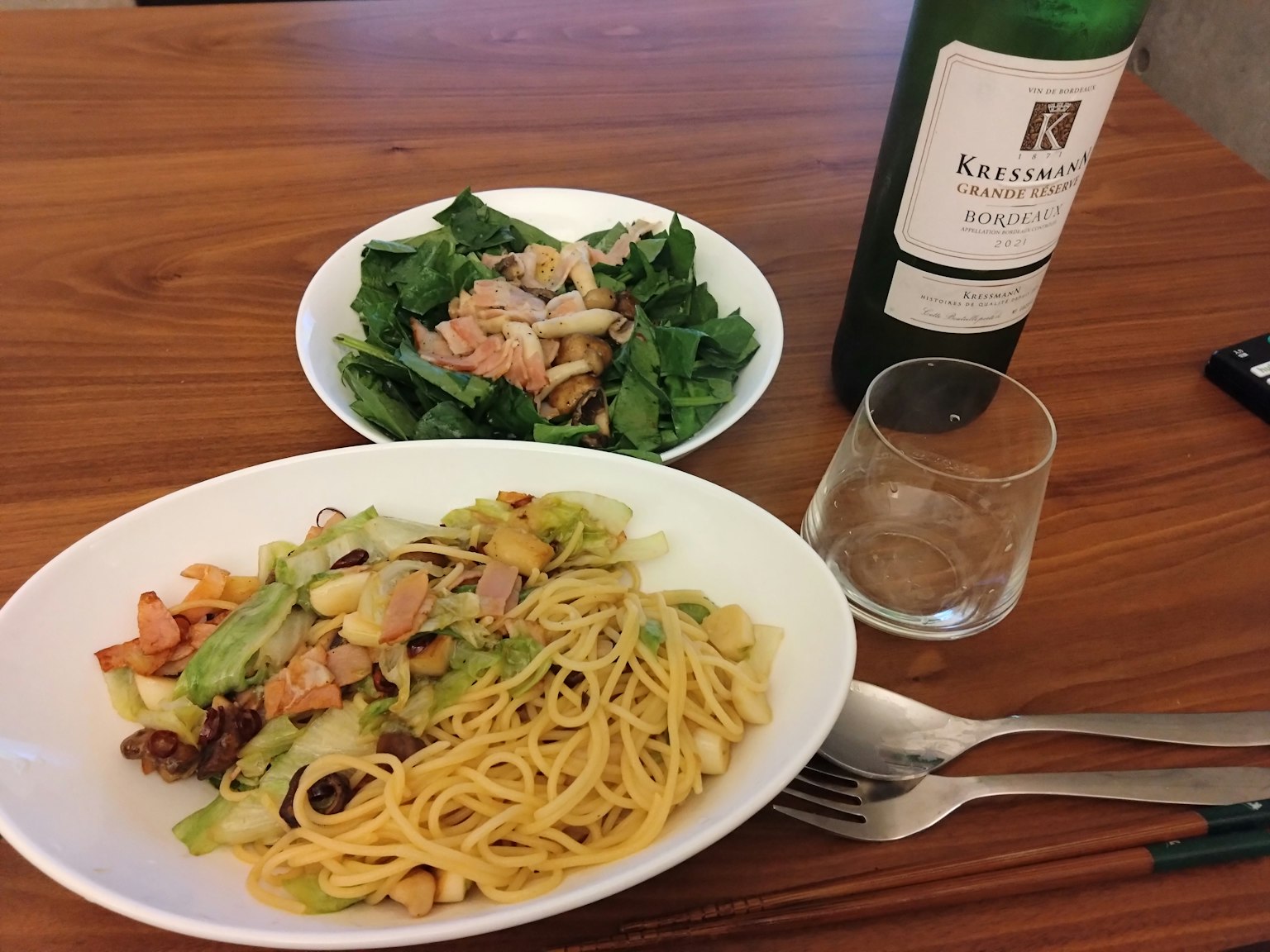 Plate of pasta with vegetables and a salad alongside a wine bottle on a wooden table