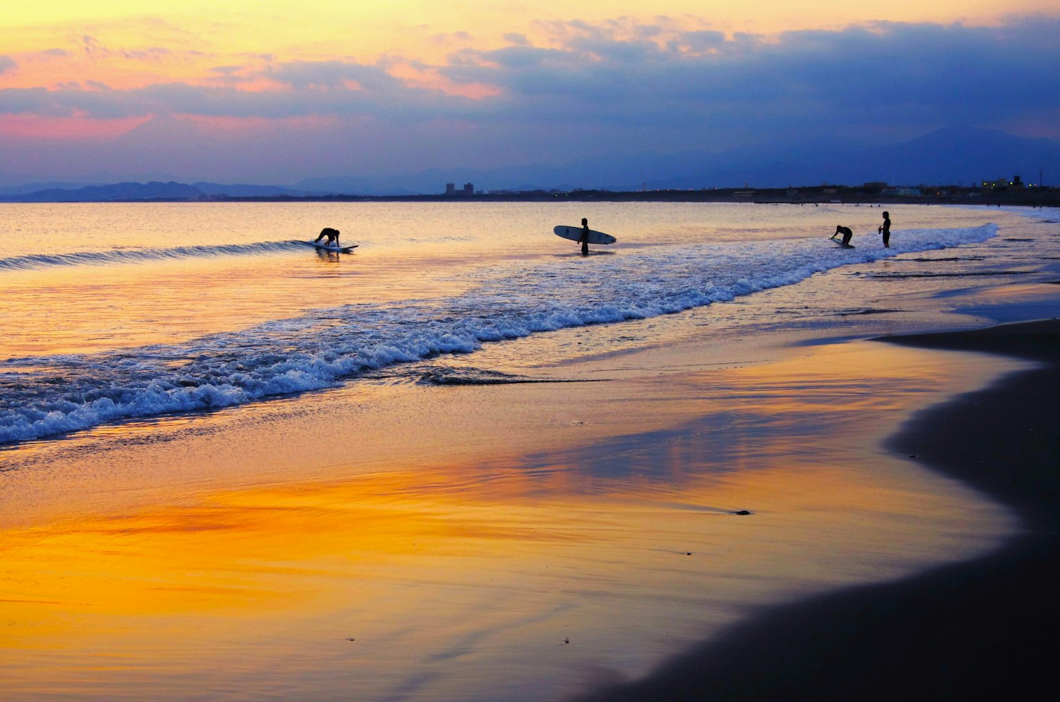 Personas surfeando en una playa al atardecer con reflejos en el agua