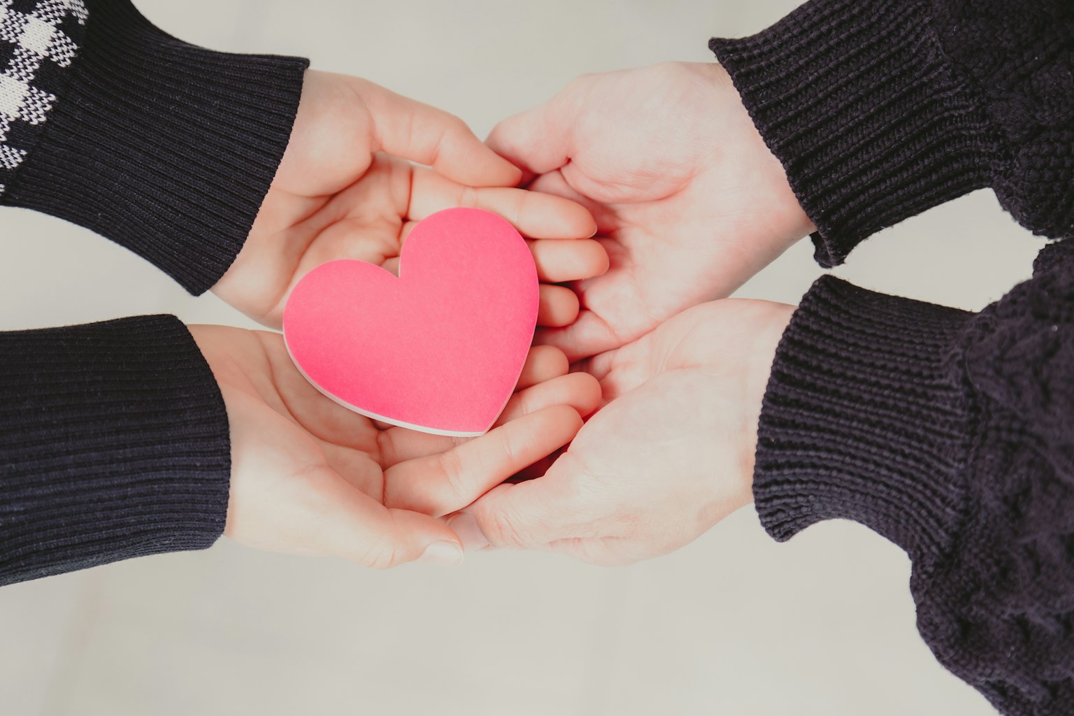 Dos manos sosteniendo una forma de corazón rosa