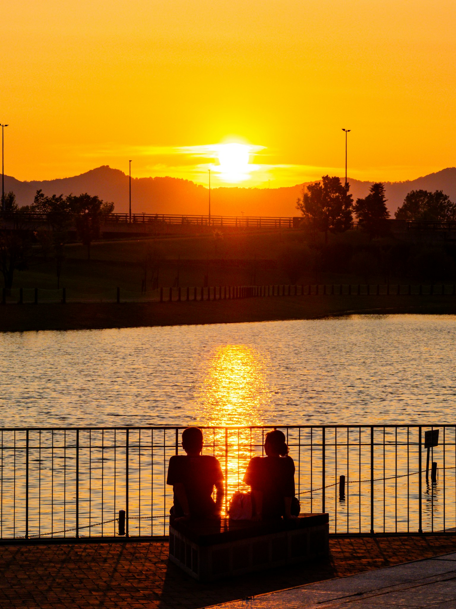 Silhouette di due persone che guardano il tramonto su un lago