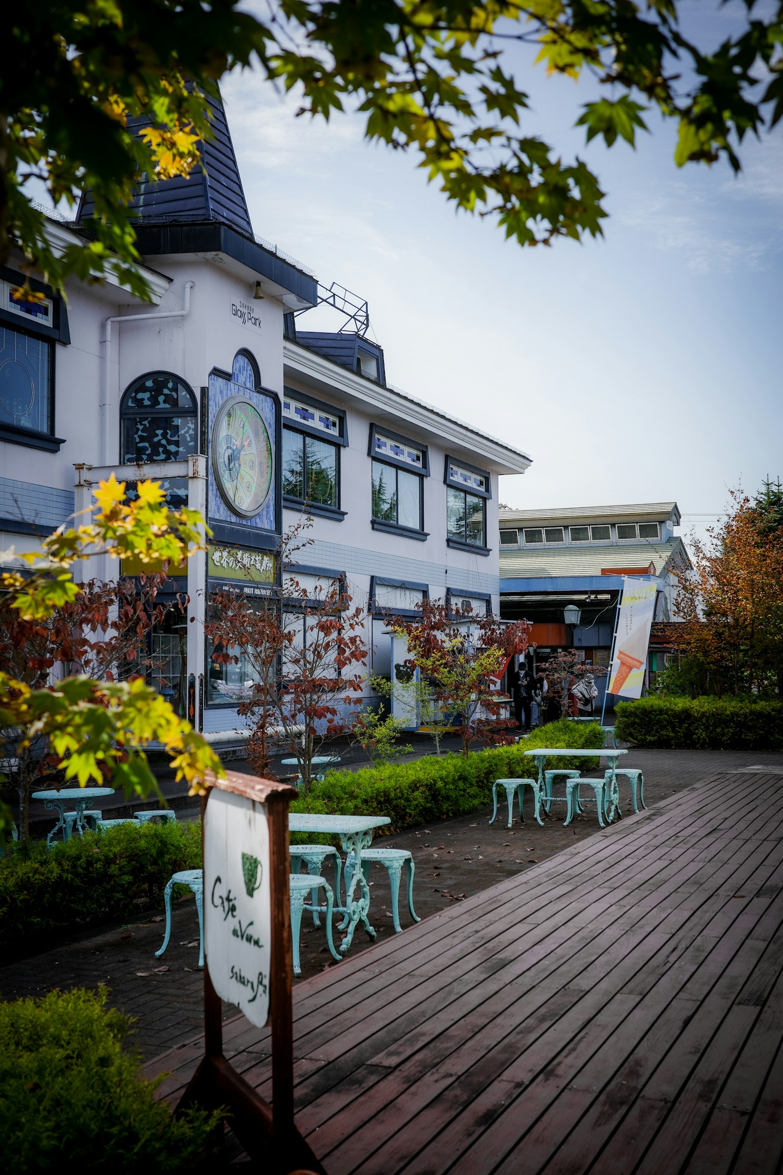 Exterior of a café with blue chairs and tables surrounded by autumn scenery
