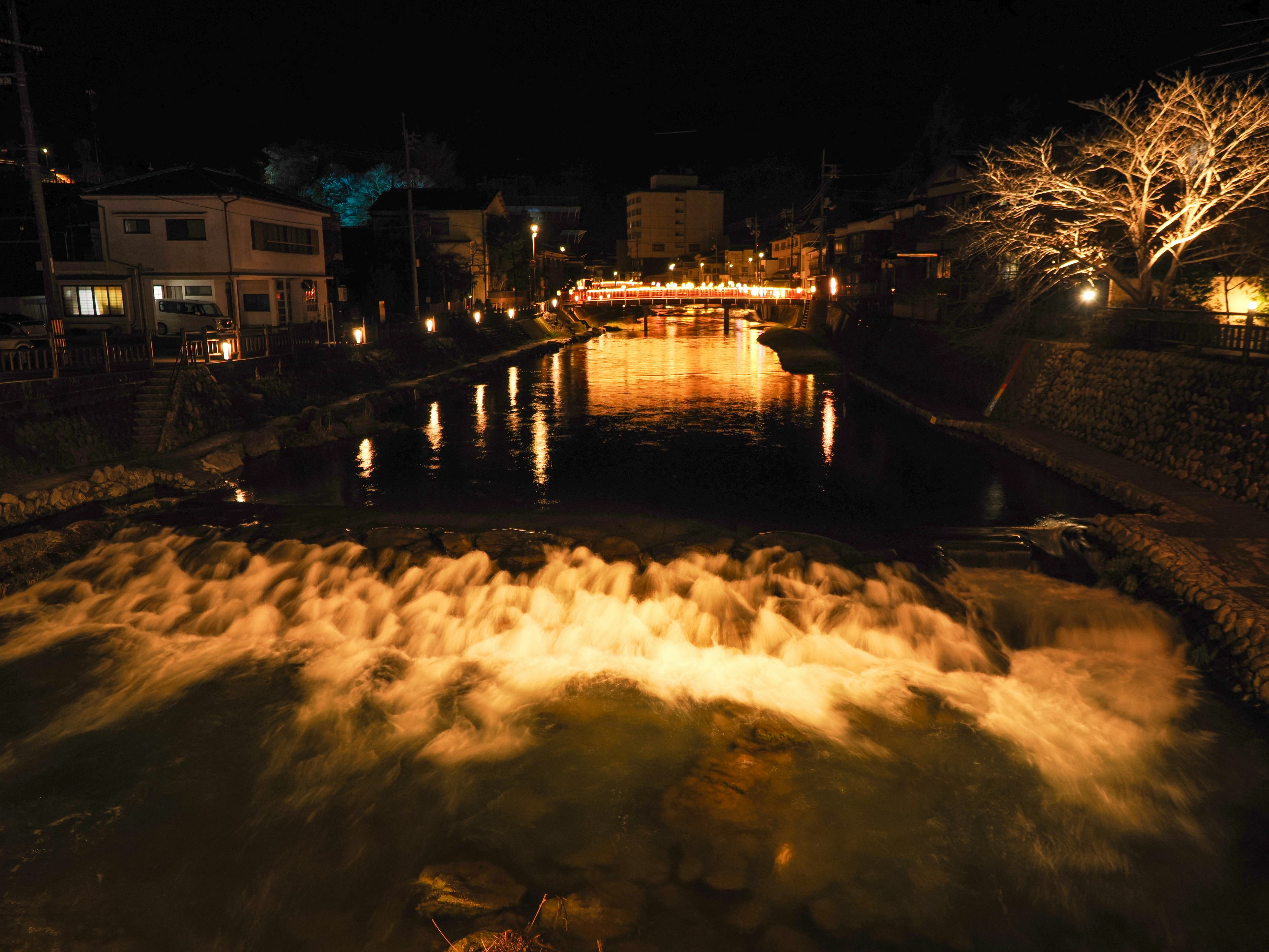 夜の川沿いに広がるライトアップされた水面と雪のような泡