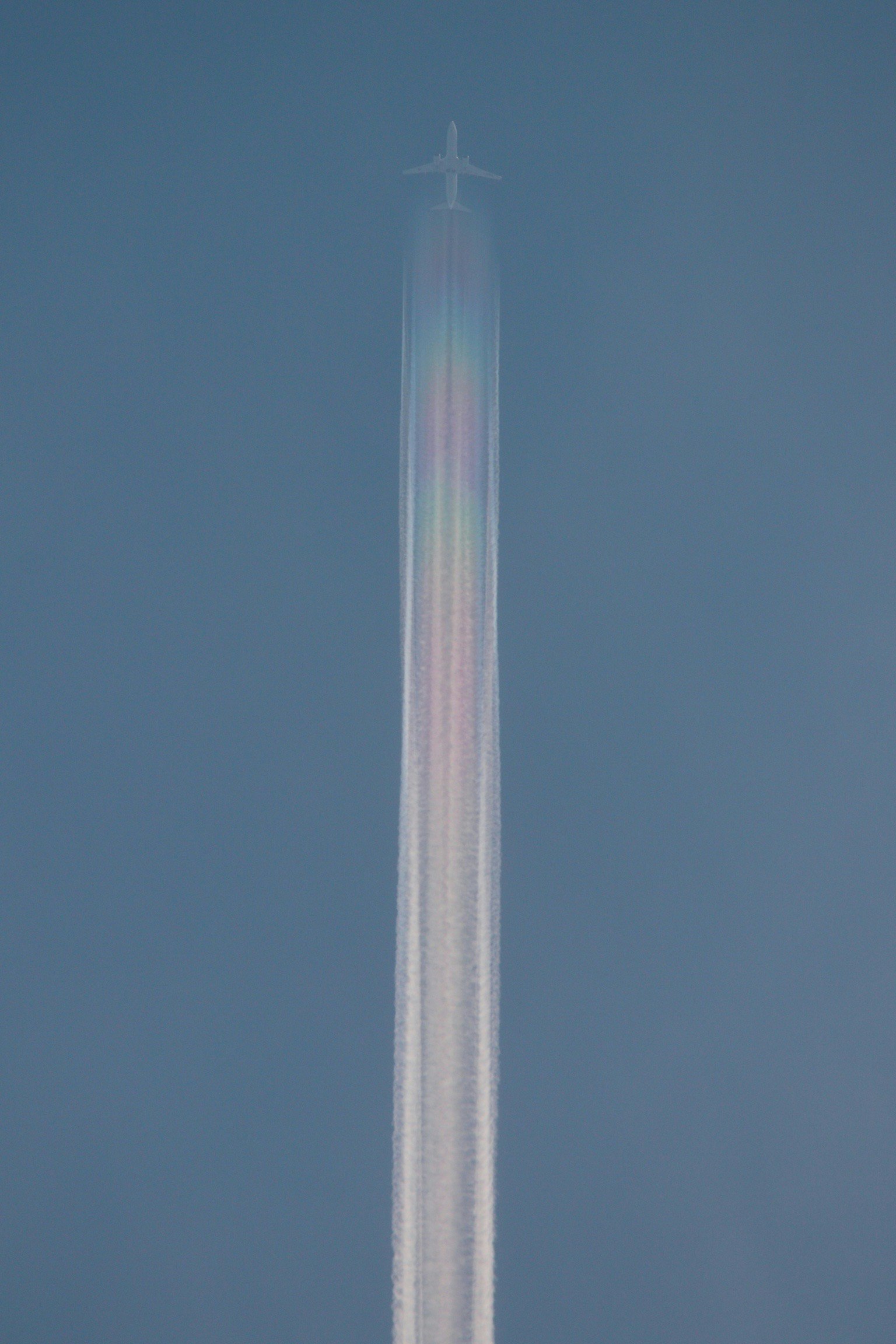 Un aereo che lascia una scia colorata in un cielo blu chiaro