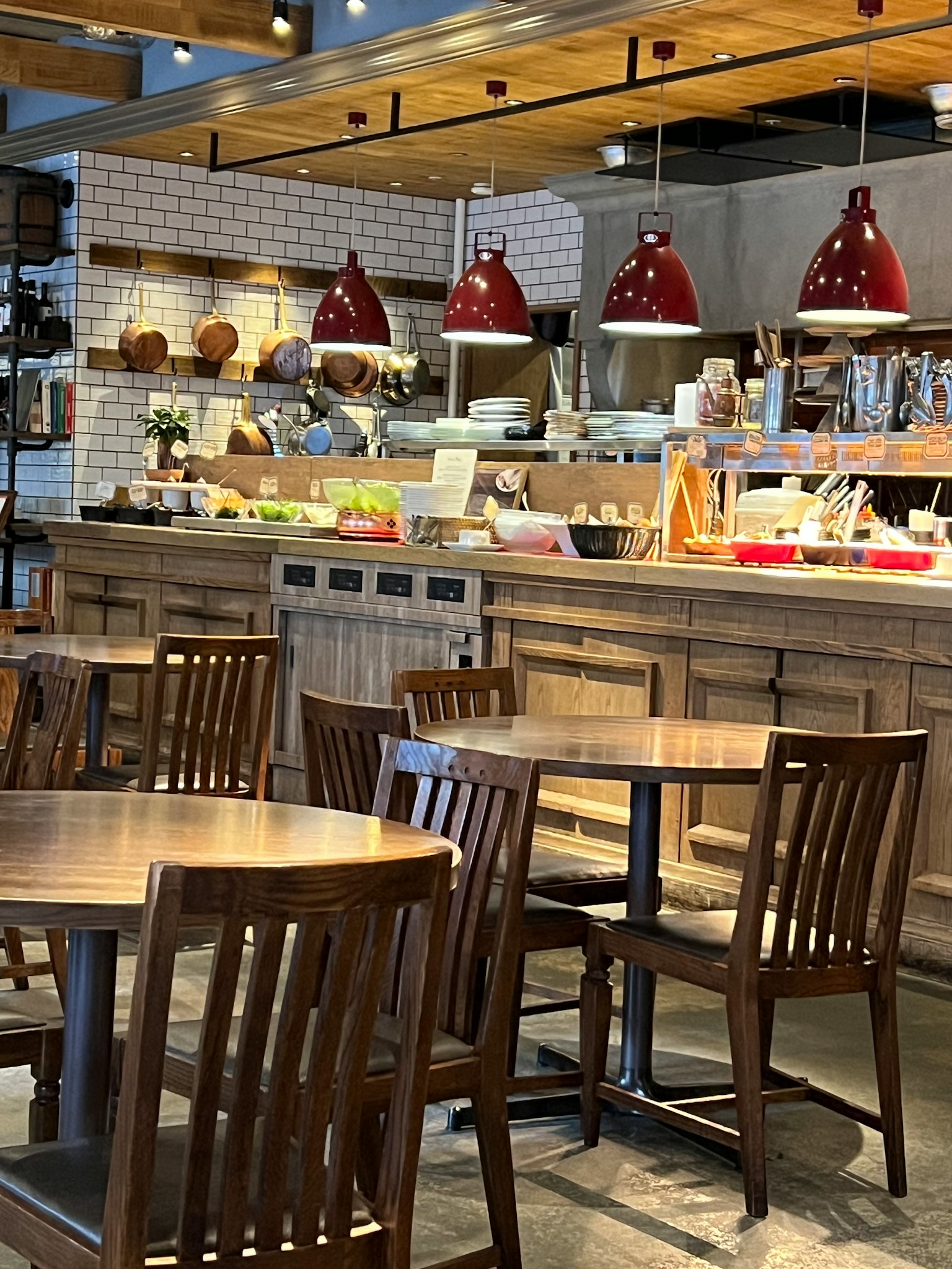 ภายในร้านกาแฟที่มีโต๊ะและเก้าอี้ไม้โคมไฟระย้าสีแดงและเคาน์เตอร์อาหาร