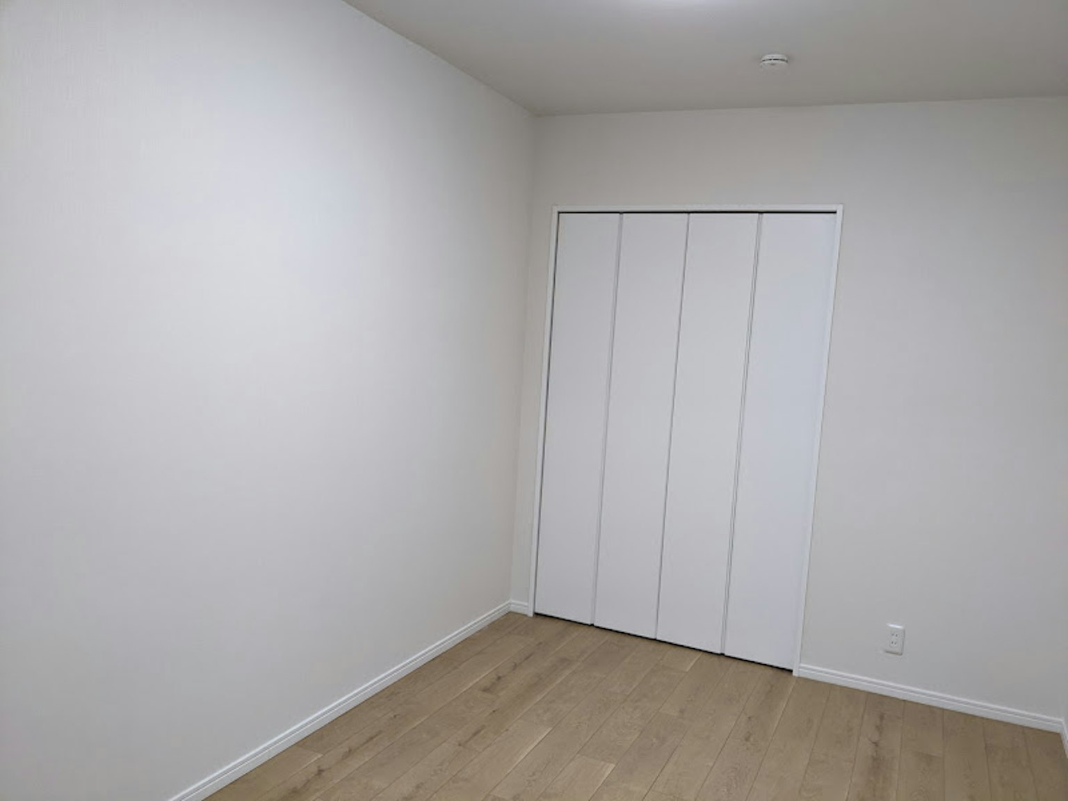 Habitación vacía con paredes blancas y suelo de madera con puertas correderas