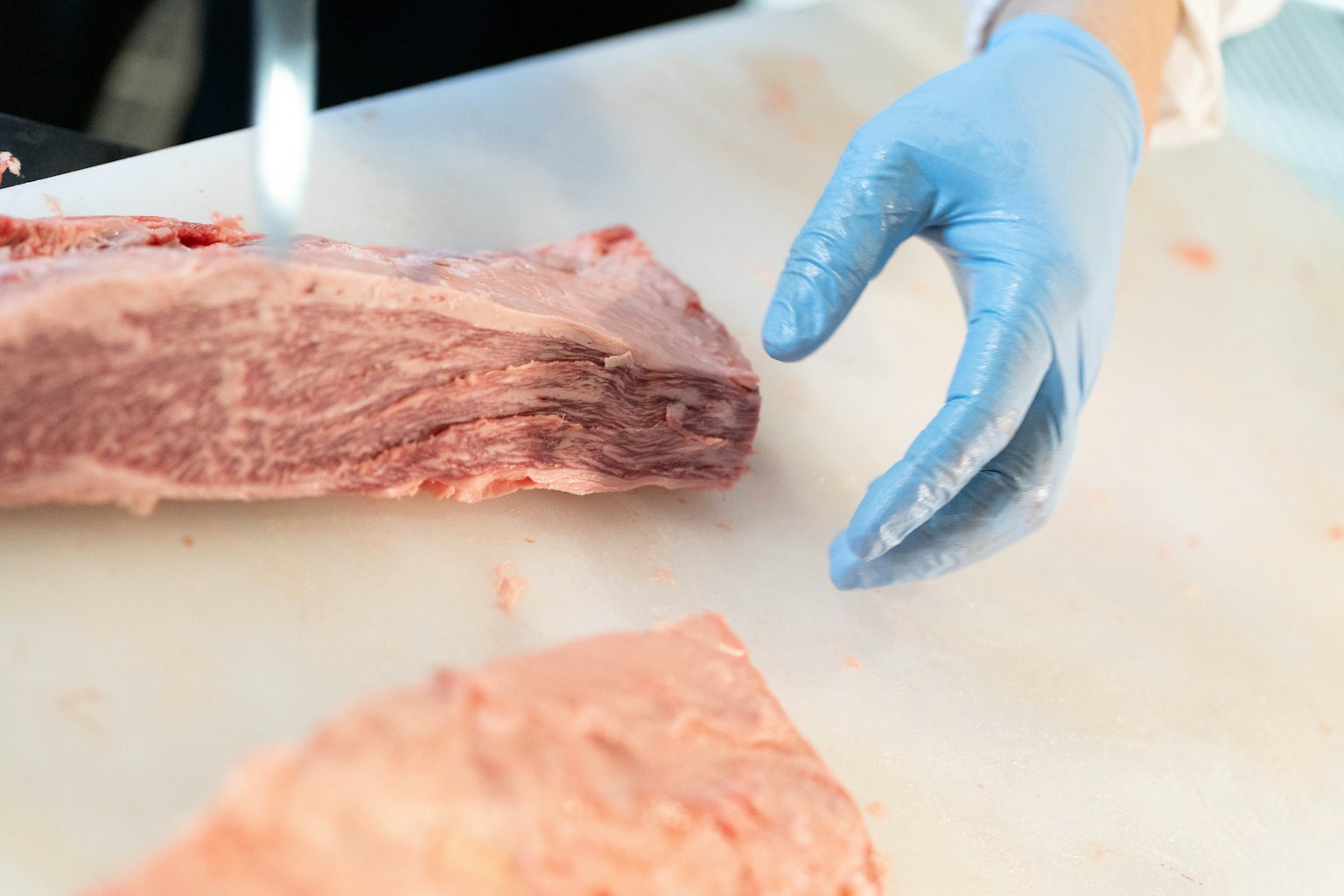 Main dans un gant bleu s'approchant d'un morceau de viande sur une planche à découper