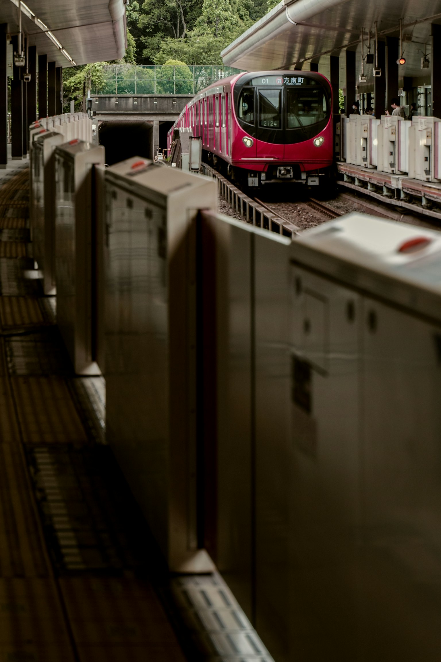 Train rouge arrivant à la station avec plateforme et tourniquets visibles