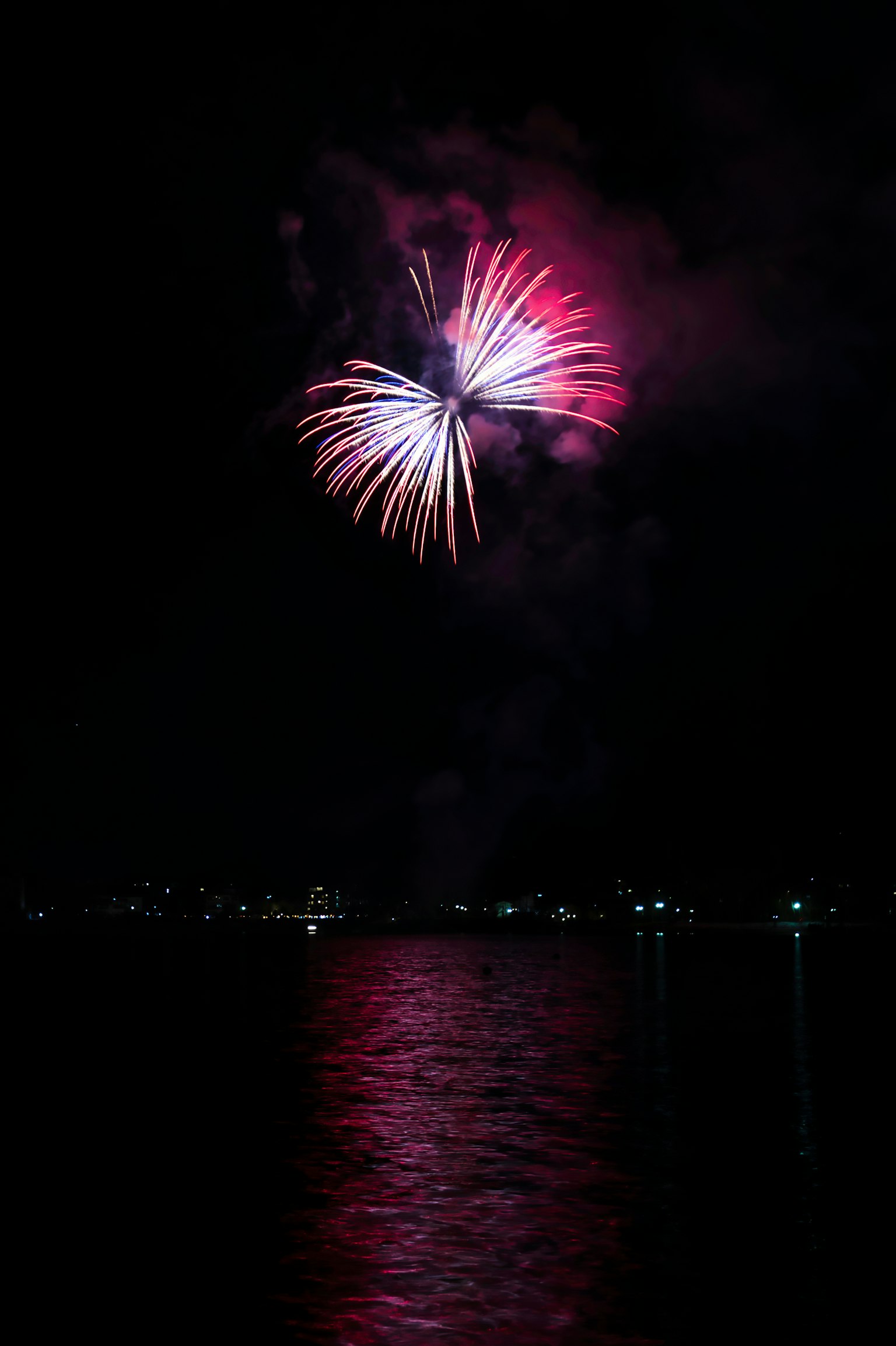 Colorful fireworks bursting in the night sky reflecting on the water