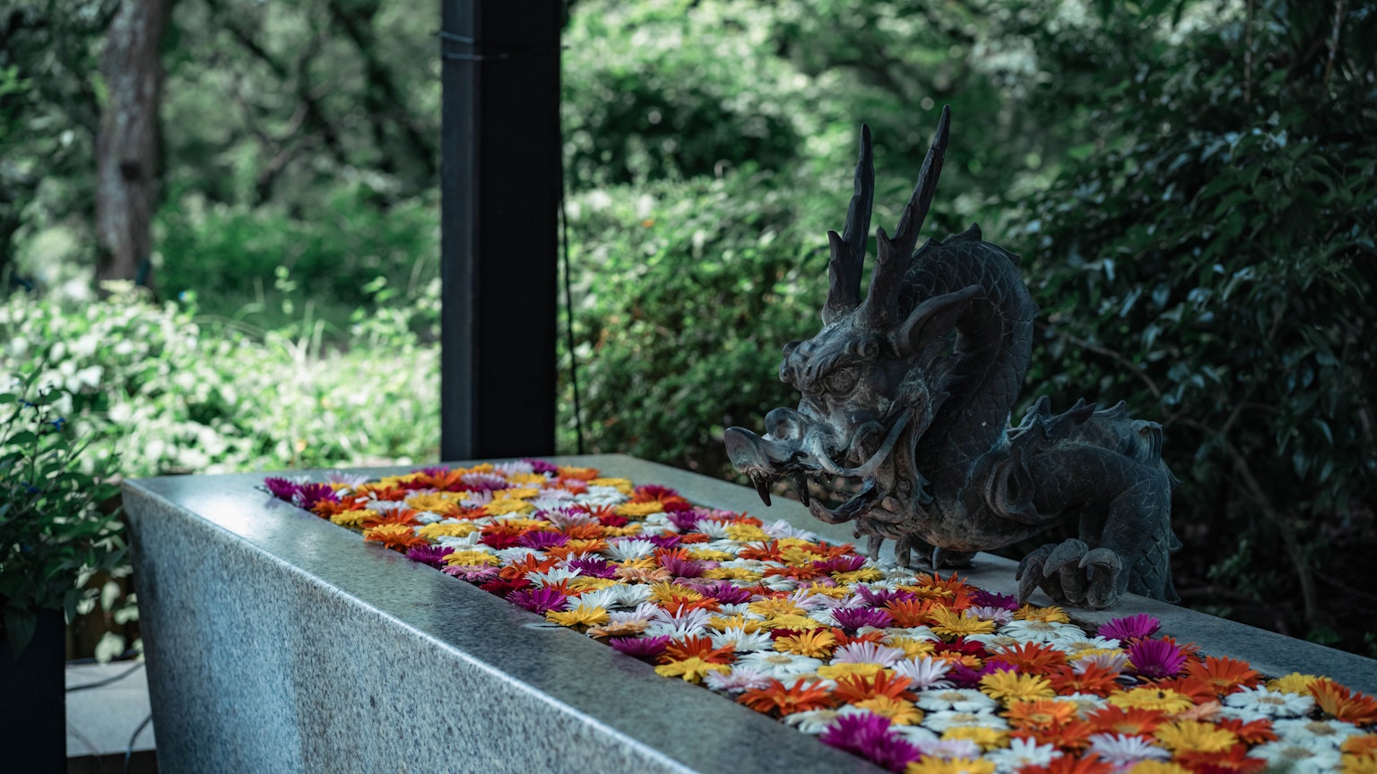 在郁郁蔥蔥的環境中，石製祭壇上裝飾著五顏六色的花朵，旁邊有神秘的雕像