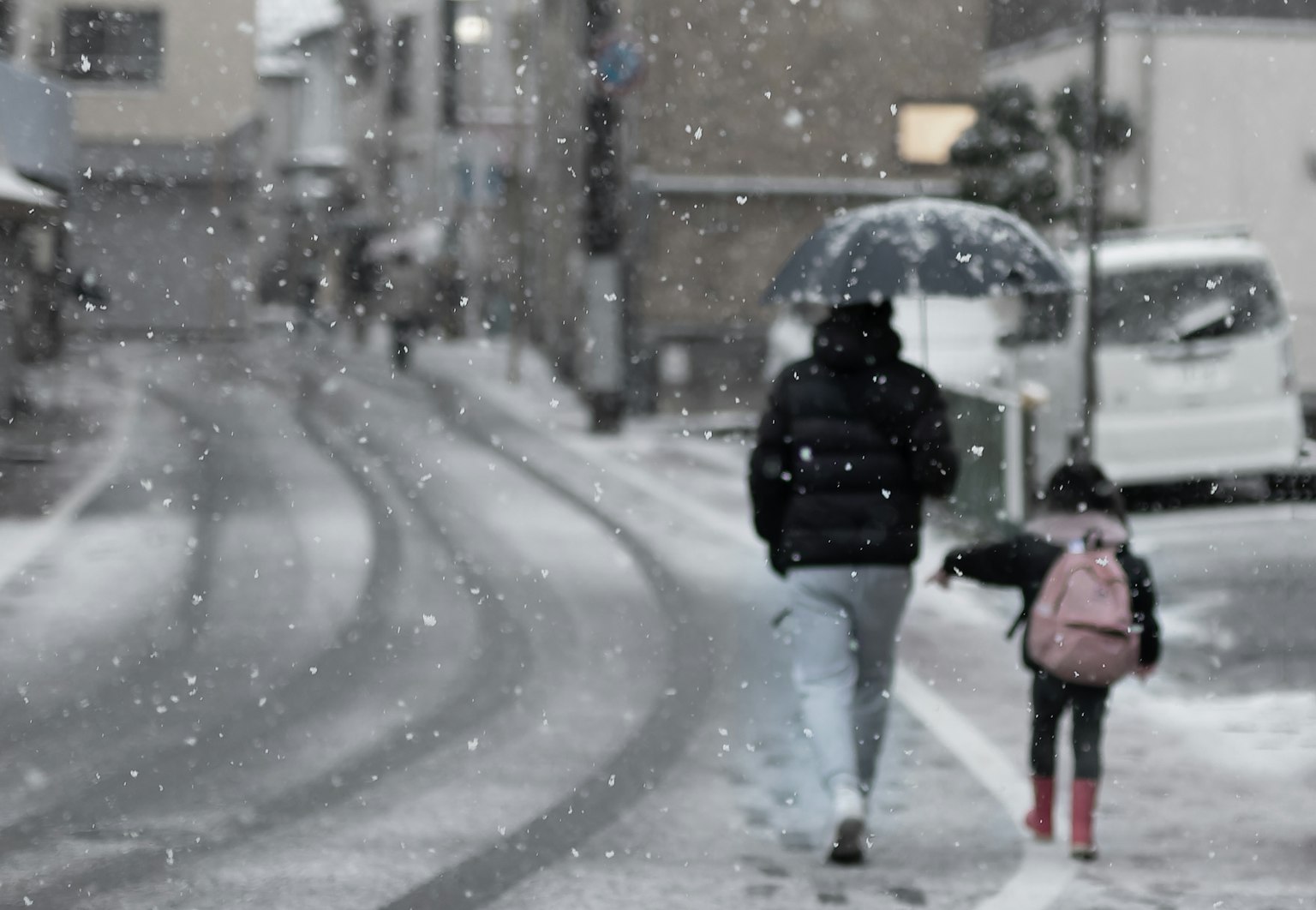 A parent and child walking in the snow on a city street