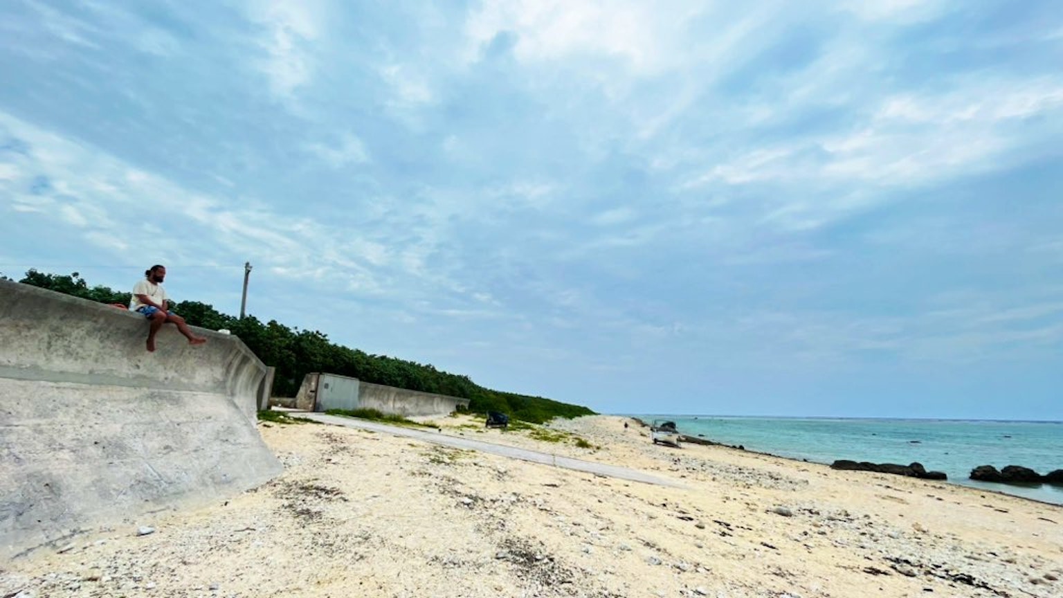 Seorang anak laki-laki duduk di dinding pantai dengan langit biru