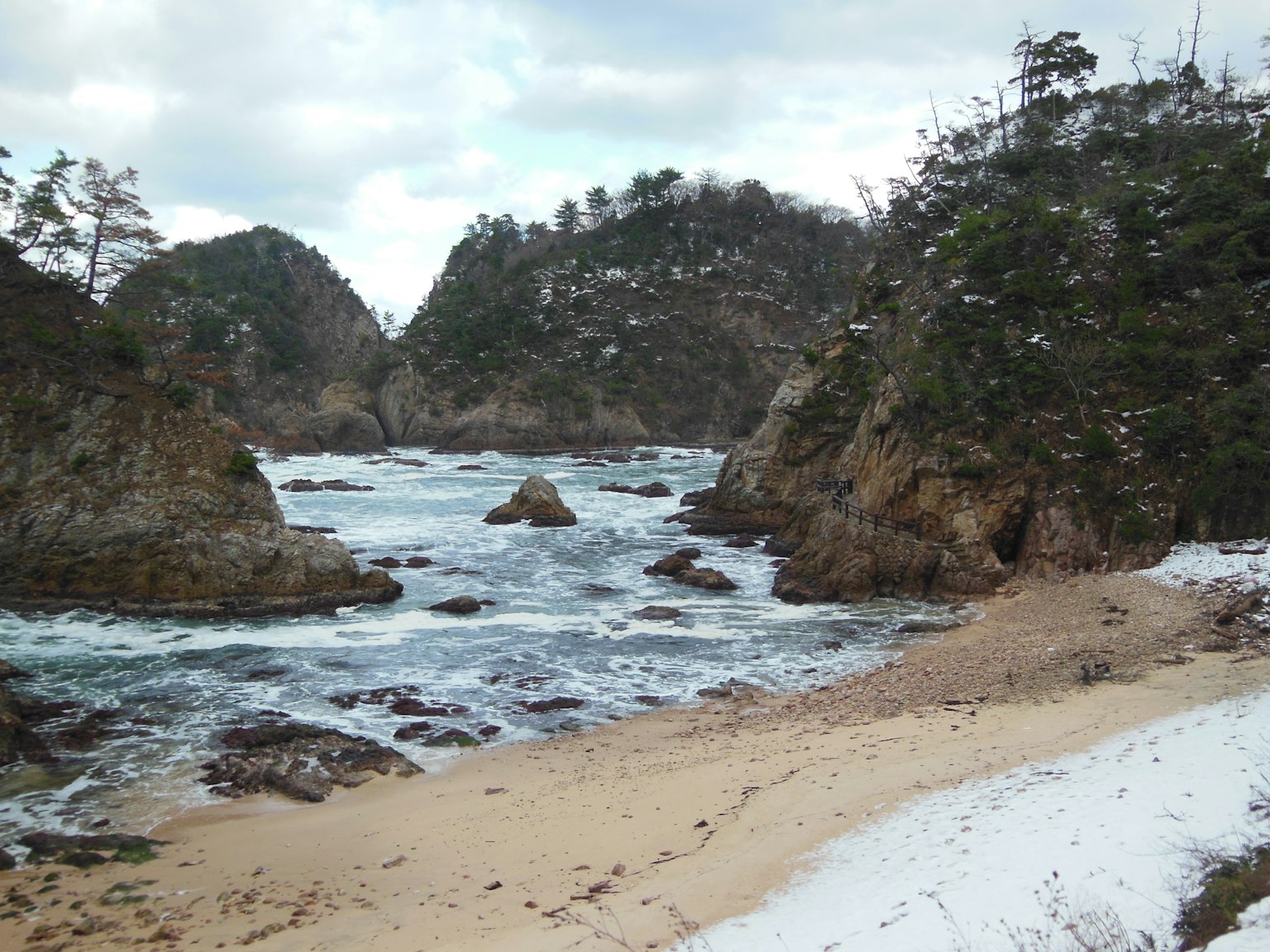 Scena di spiaggia innevata con costa rocciosa e onde