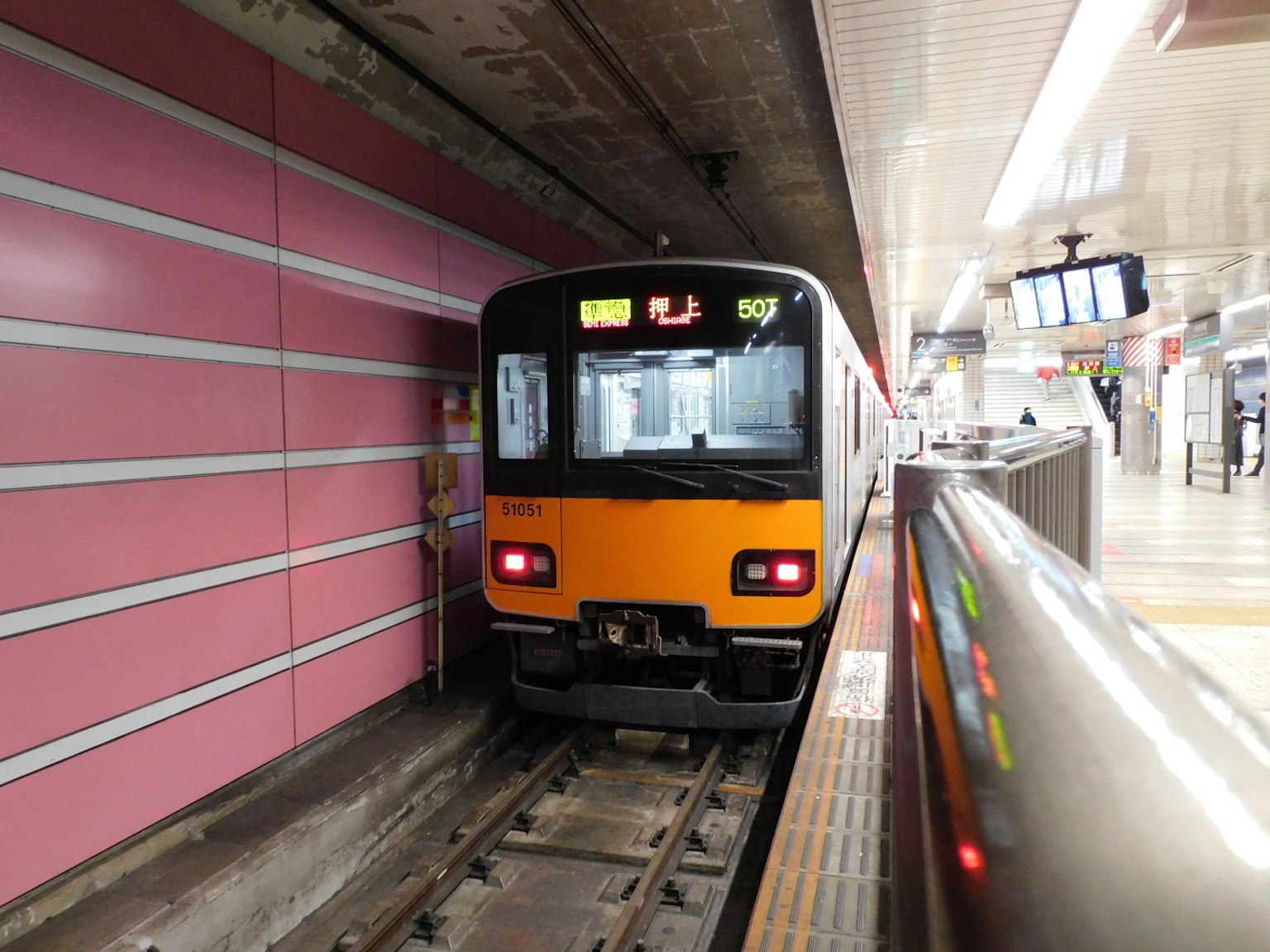 Treno arancione fermo in una stazione con muri rosa