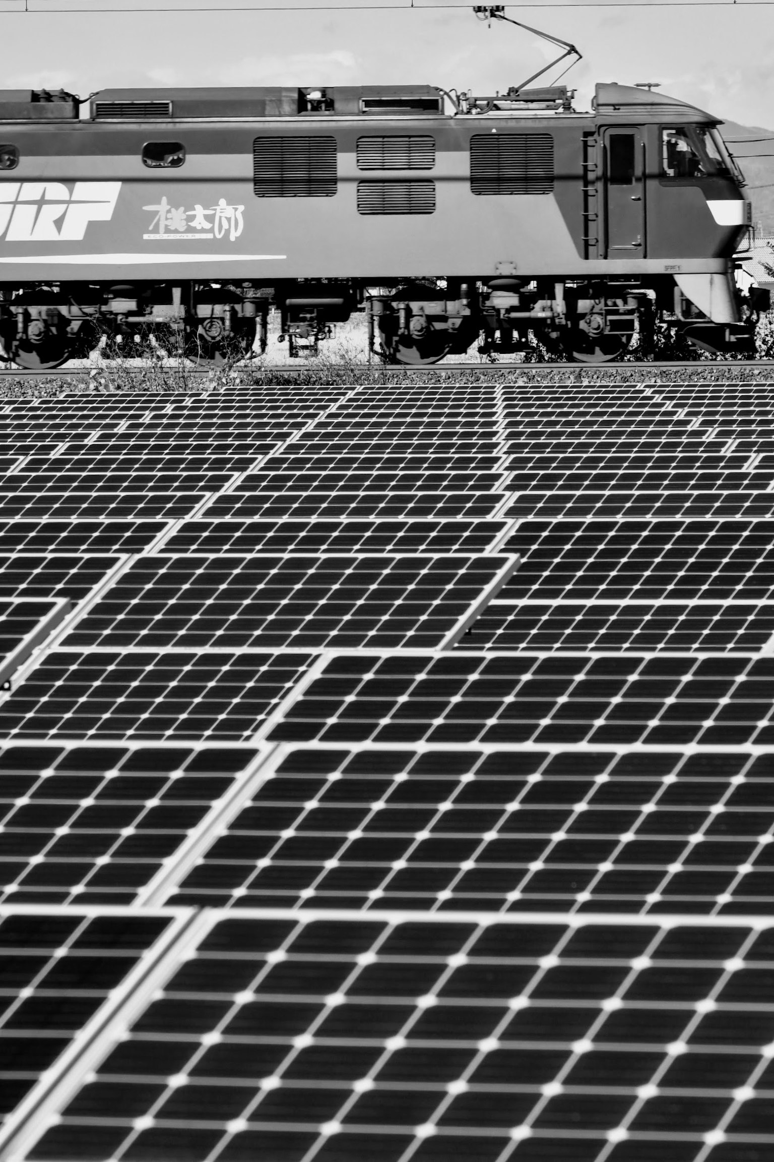 Train running over solar panels in a black and white setting
