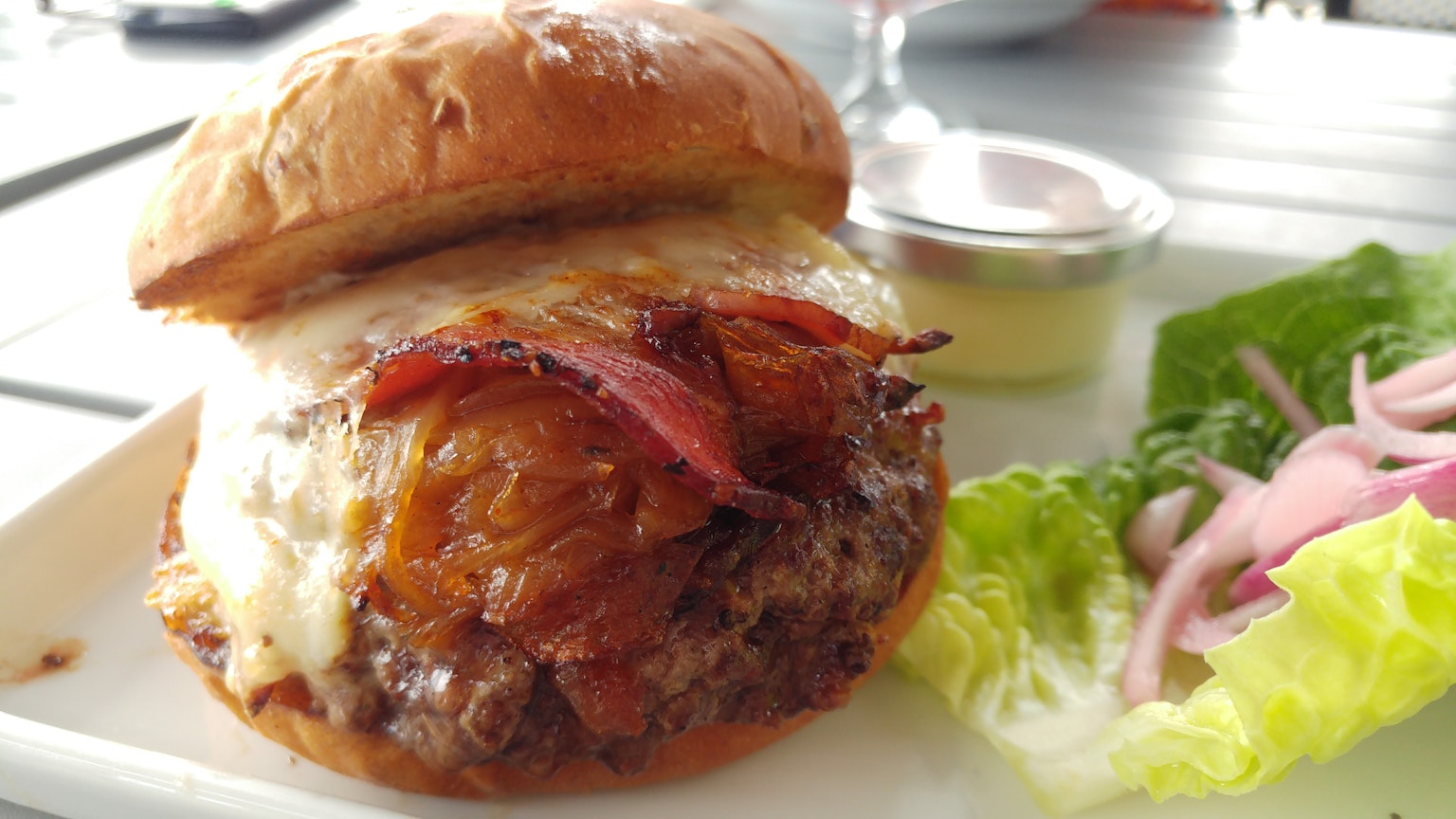 Una hamburguesa deliciosa con capas de carne y queso y tocino crujiente encima servida con lechuga y cebollas