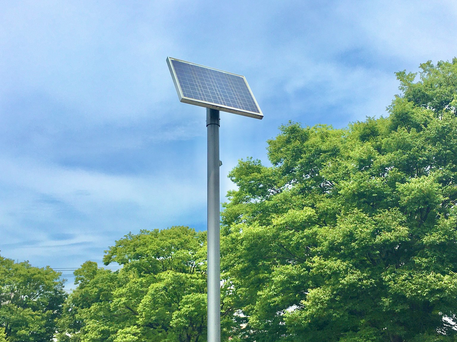 Pannello solare montato su un palo con alberi verdi sotto un cielo blu