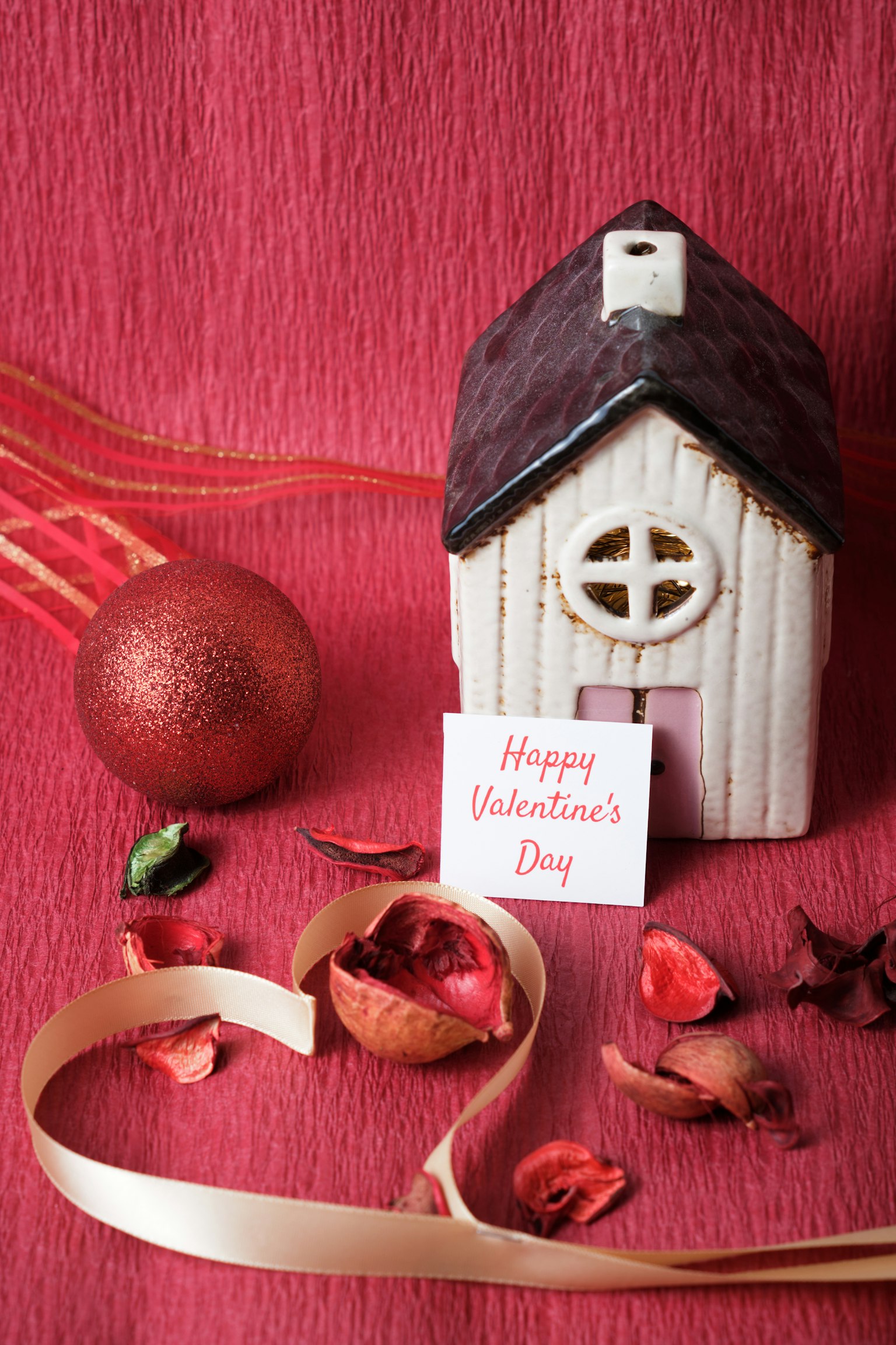 Figur rumah keramik dengan kartu Hari Valentine di latar belakang merah