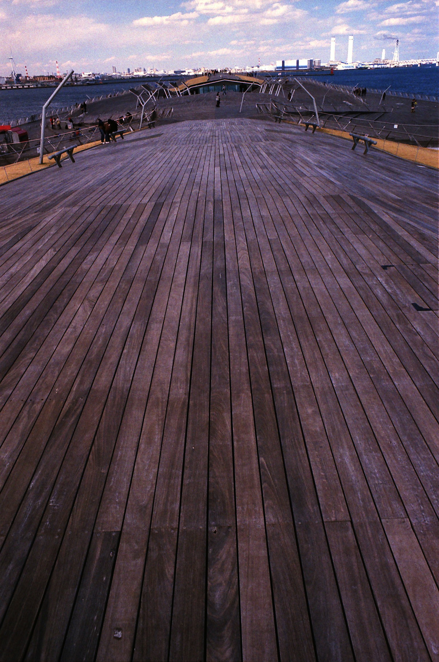 Wooden deck extending into the distance with a cloudy sky and distant buildings