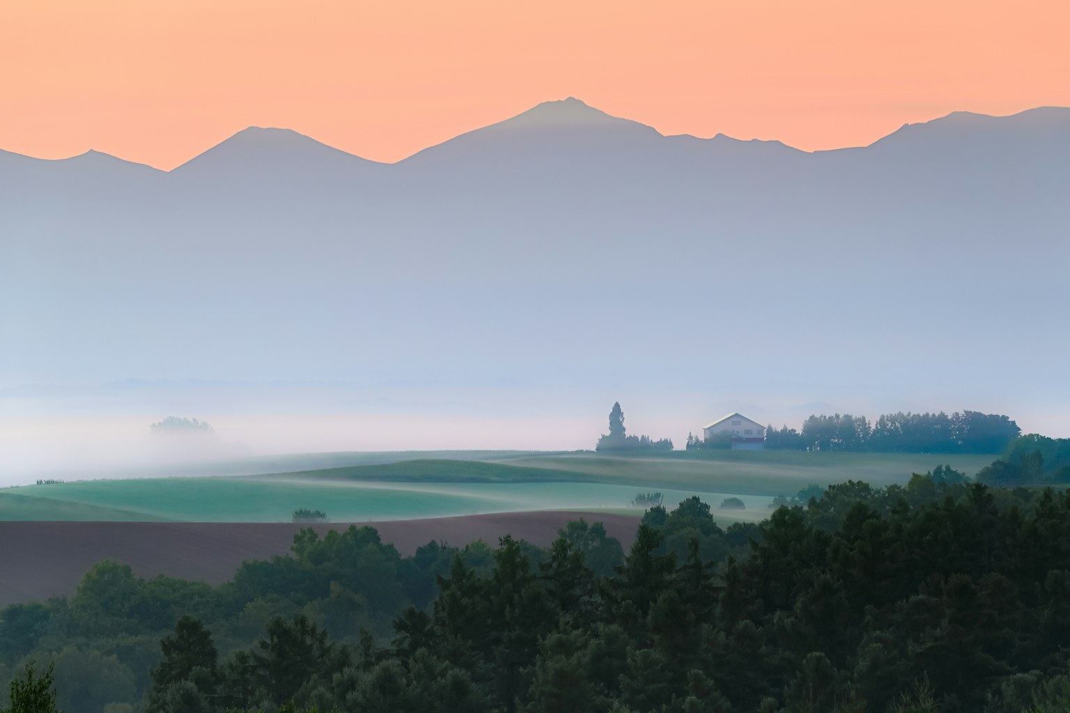 霧に包まれた山々と広がる農地の風景 朝焼けの空が美しい