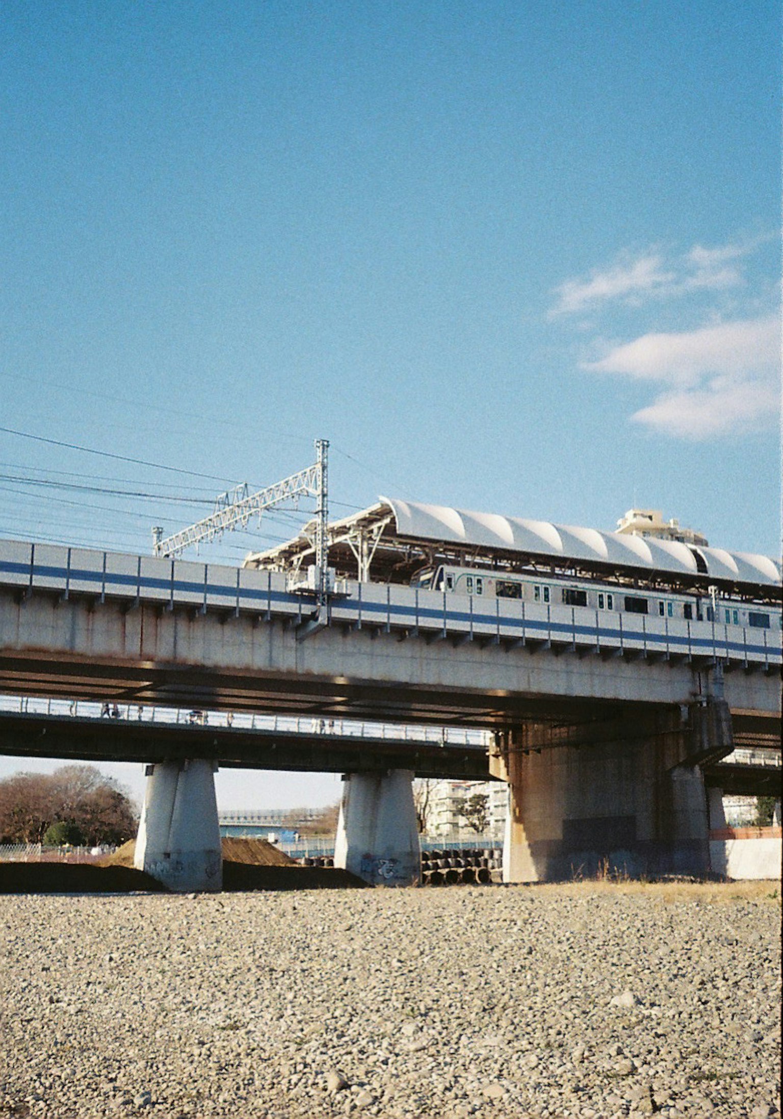 Eine Ansicht eines erhöhten Zuges, der unter einem blauen Himmel fährt und die Eisenbahnstruktur und die umliegende Natur zeigt