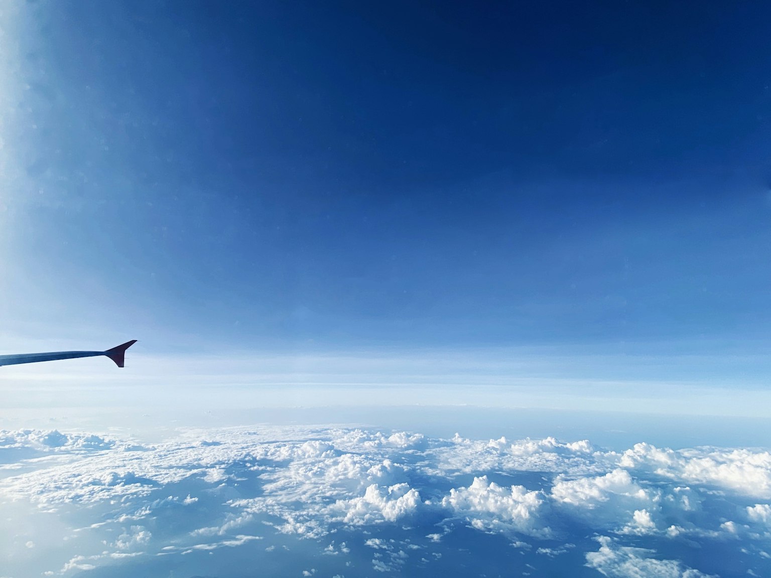 Flügel eines Flugzeugs vor blauem Himmel und Wolken