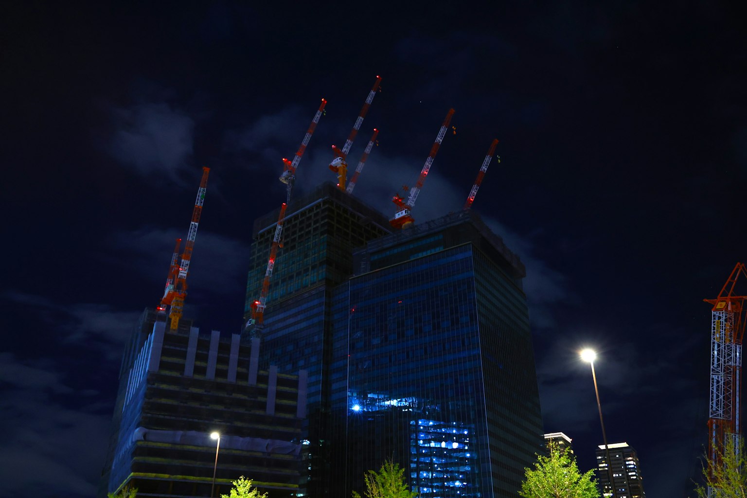 Chantier de construction d'un gratte-ciel illuminé la nuit avec des grues rouges et blanches en évidence