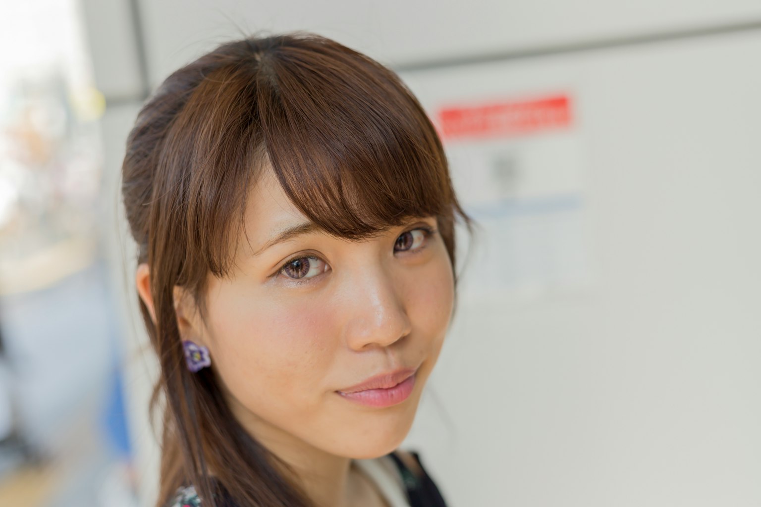 Portrait of a woman with brown hair and purple earrings against a white wall