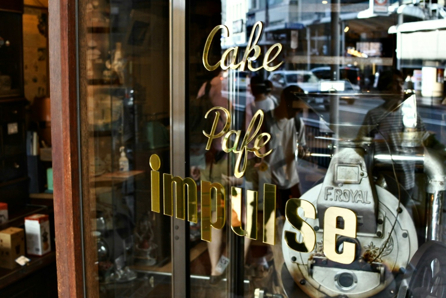Entrada del Café Impulse con letras doradas y reflejos de personas