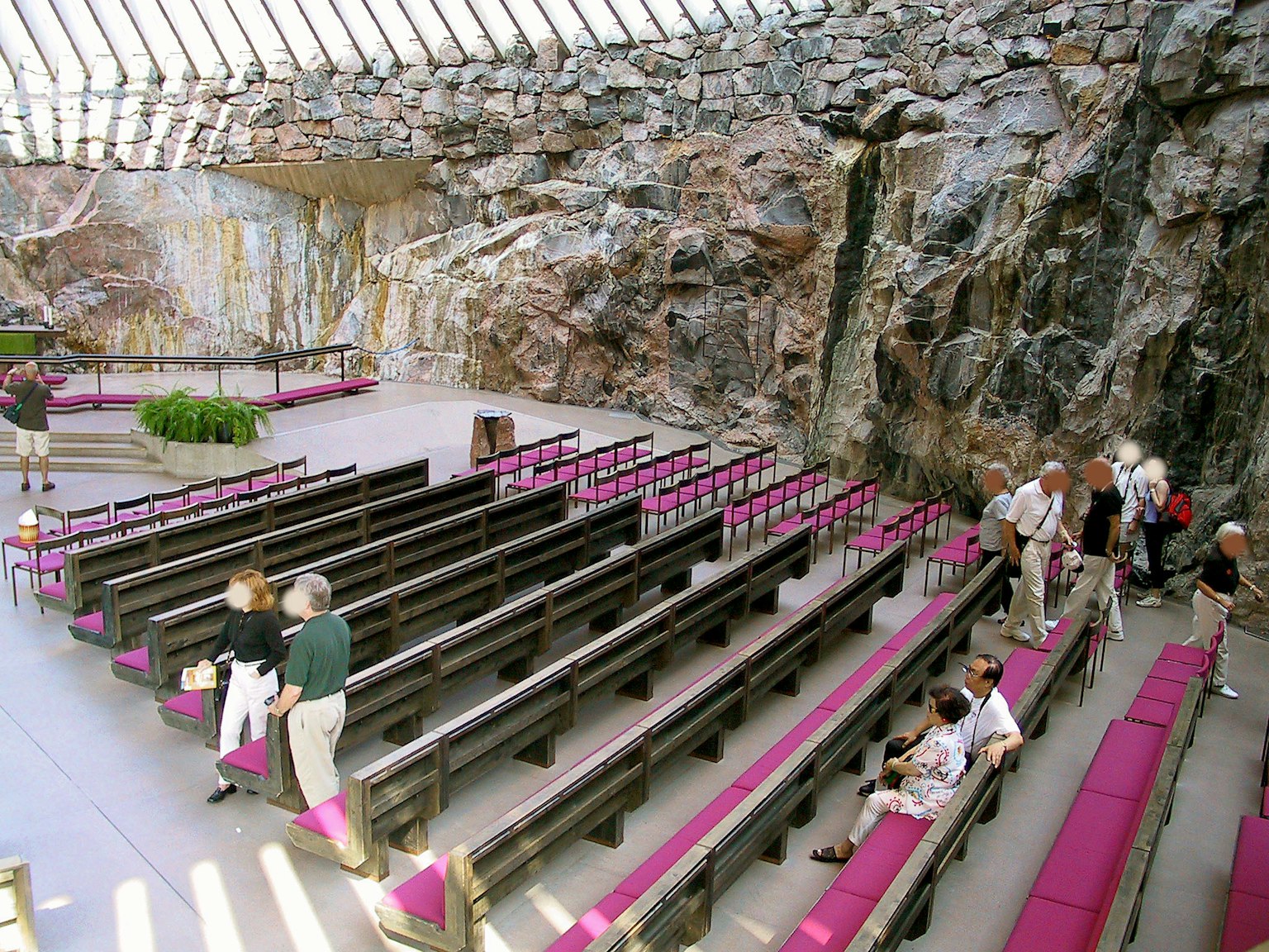 Innenraum einer Felsen-Kirche mit Bänken und Besuchern