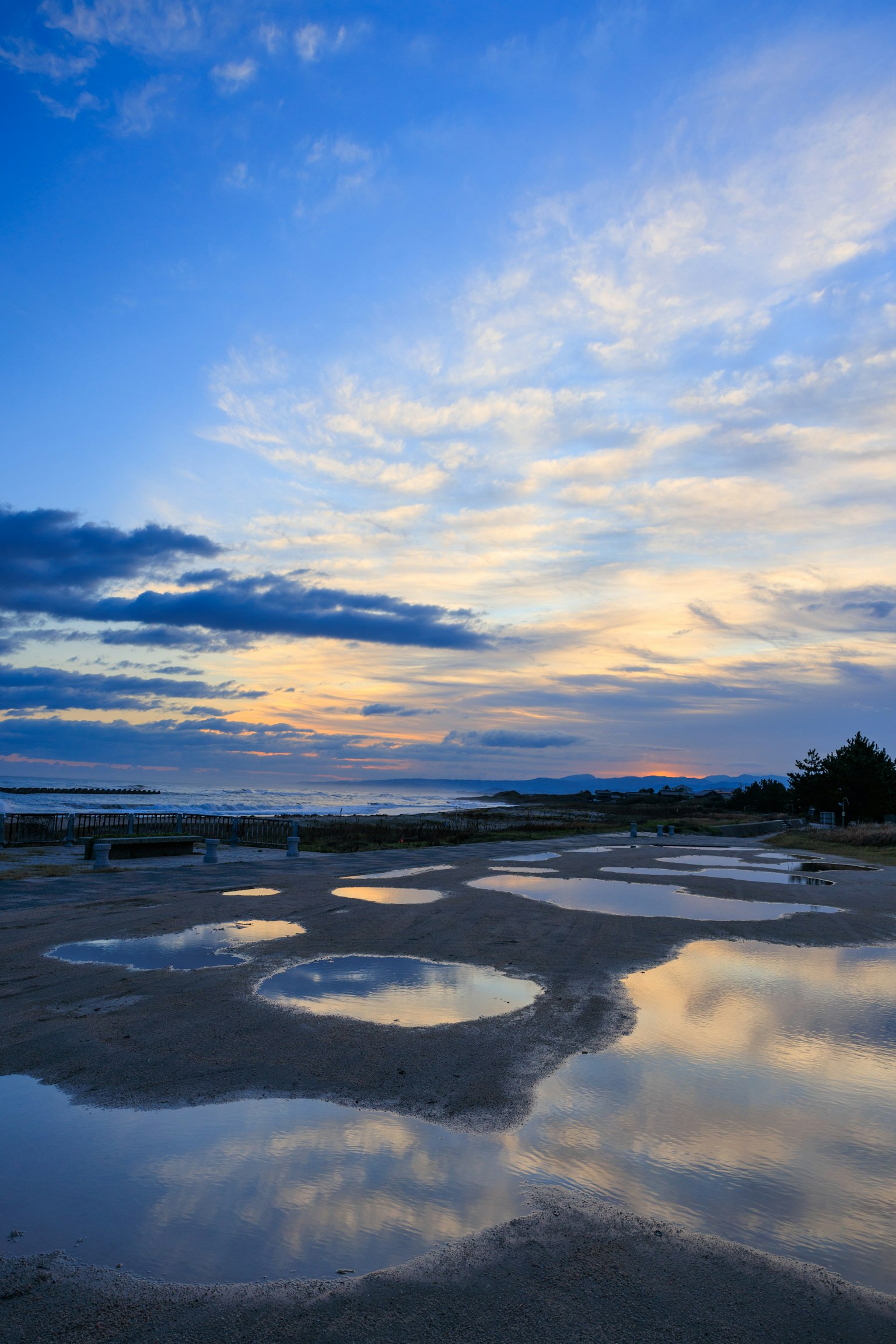 Pemandangan pantai dengan genangan yang memantulkan langit biru dan awan