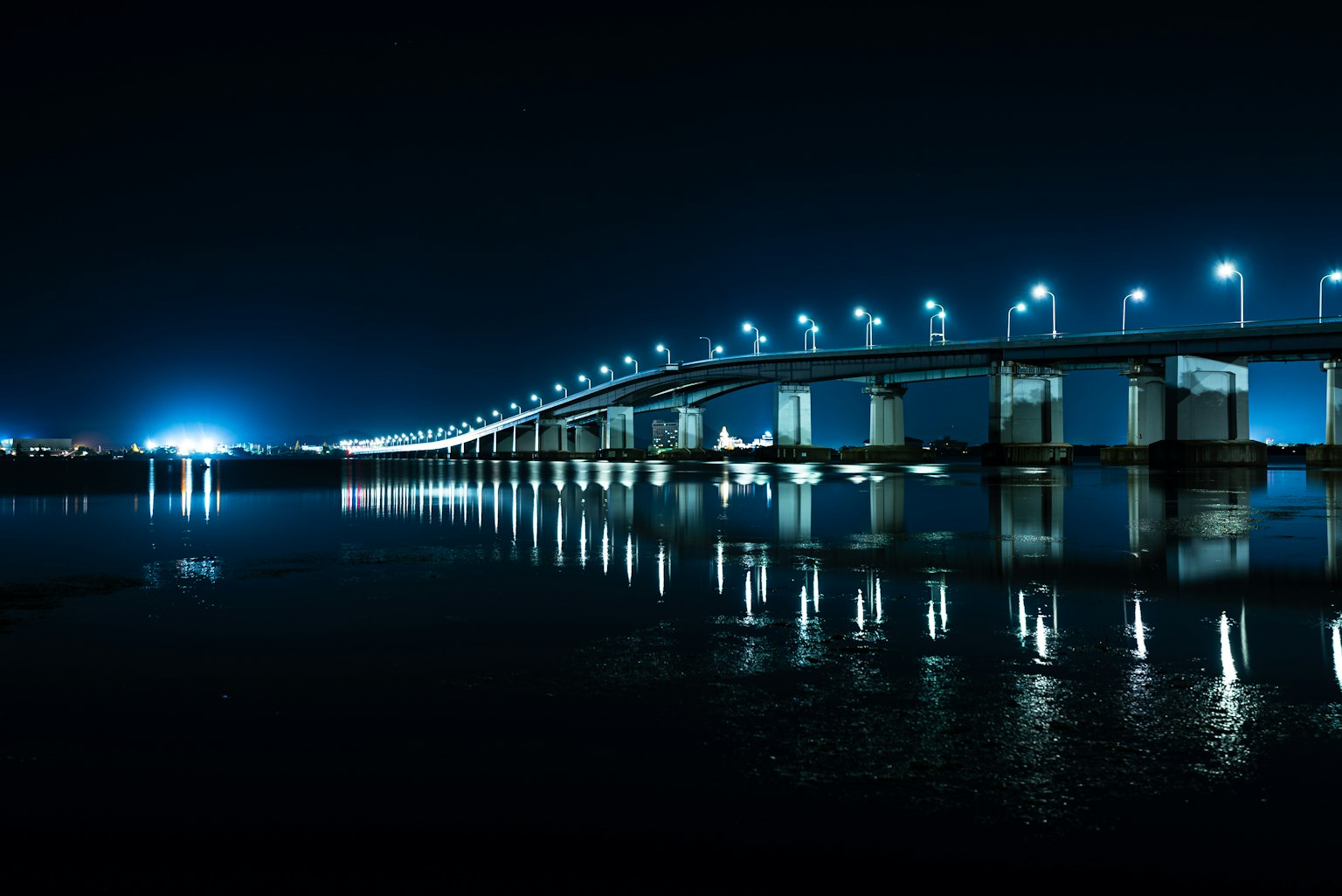 Jembatan yang diterangi memantul di sungai di malam hari
